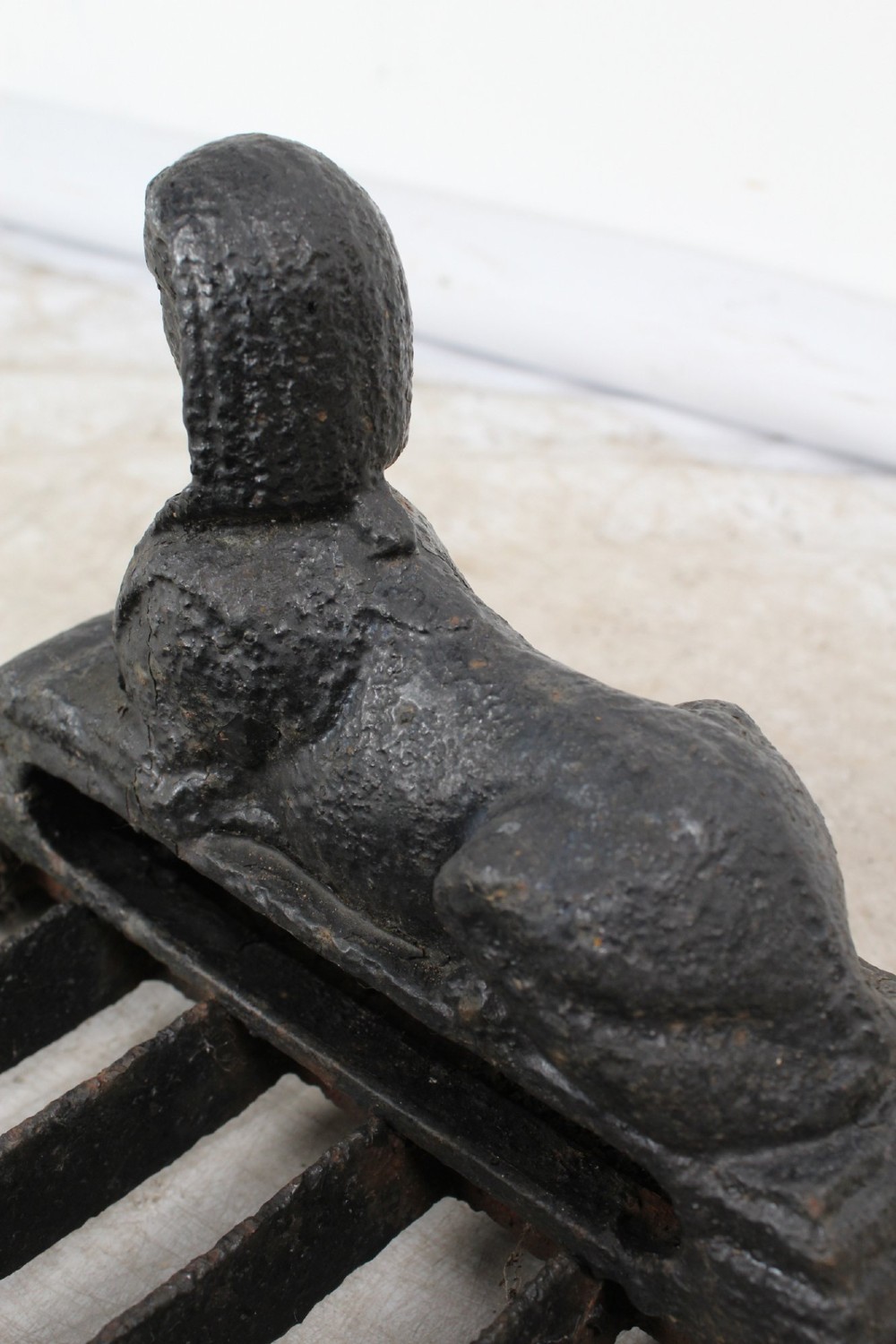 A dark cast iron boot scraper featuring twin sphinx figures flanking a central slatted grate set upon a decorative moulded base. View XII