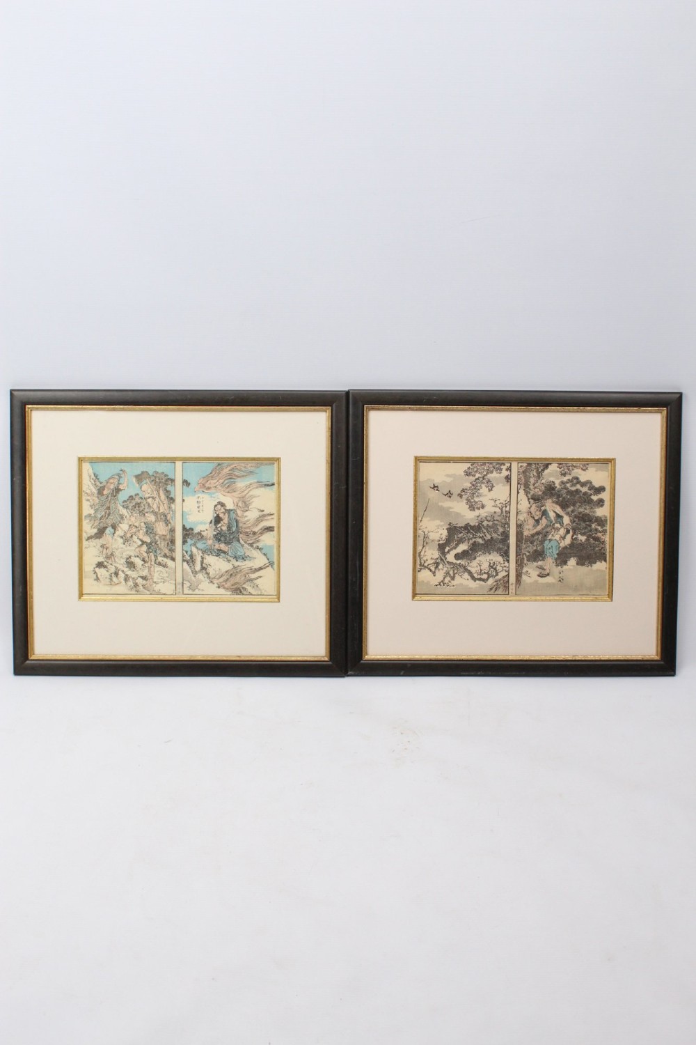 A pair of framed Japanese woodblock prints featuring detailed figurative and landscape illustrations mounted in cream mats within dark wooden frames. View II