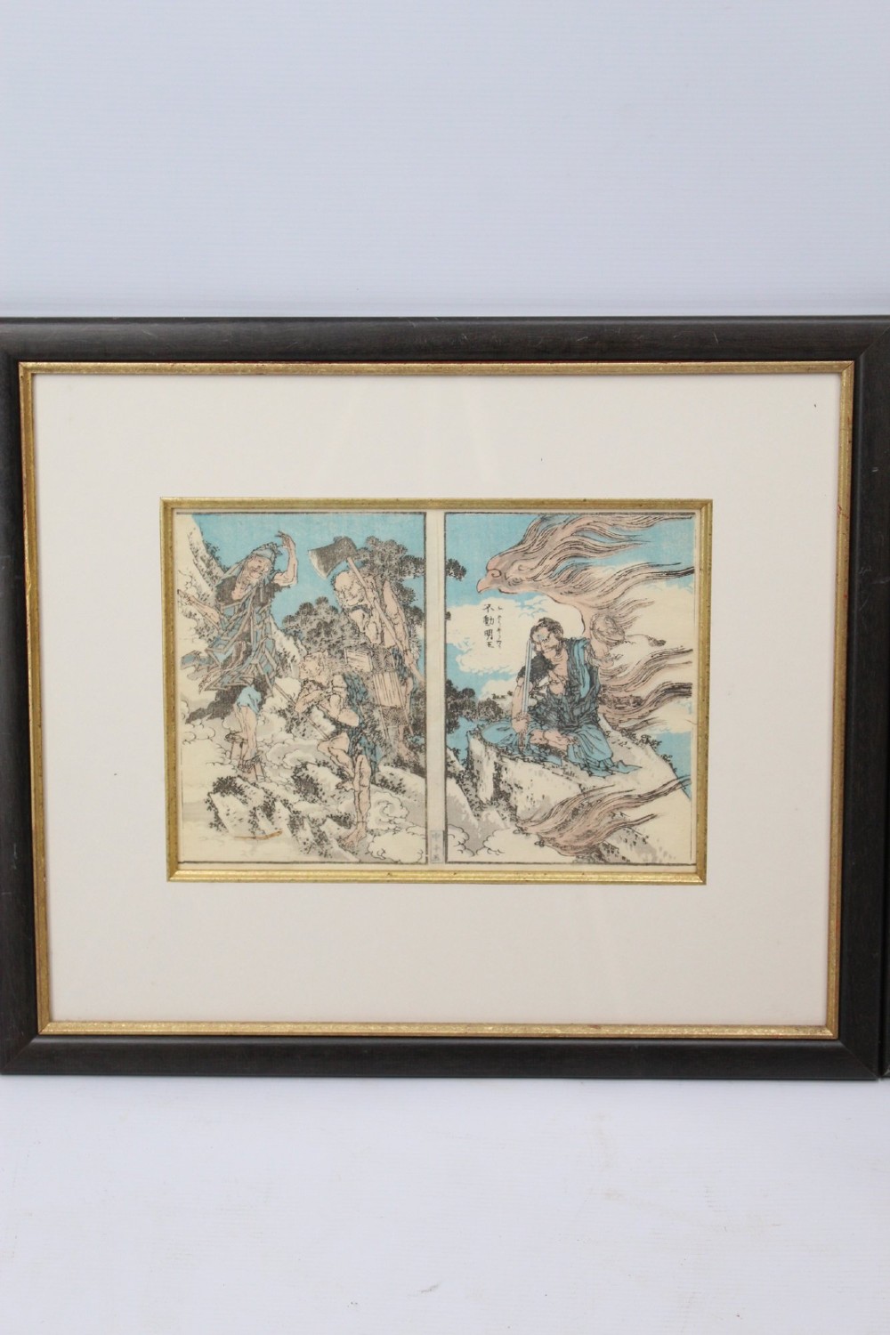 A pair of framed Japanese woodblock prints featuring detailed figurative and landscape illustrations mounted in cream mats within dark wooden frames. View III