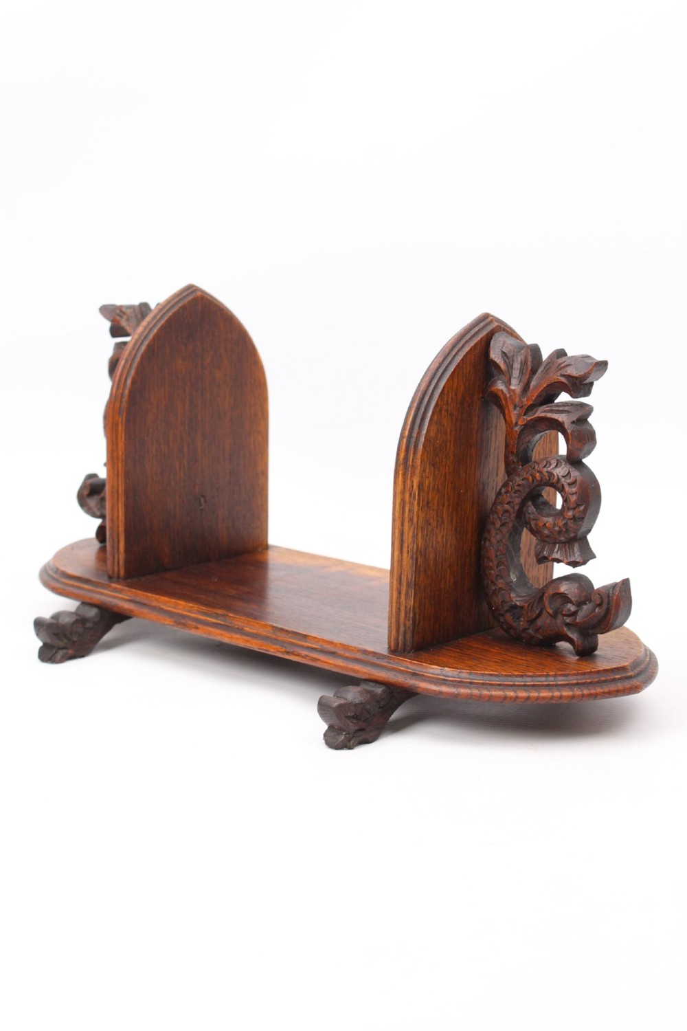 A dark oak desktop book stand featuring pointed arch uprights, carved mythical creature side accents, and scroll feet.