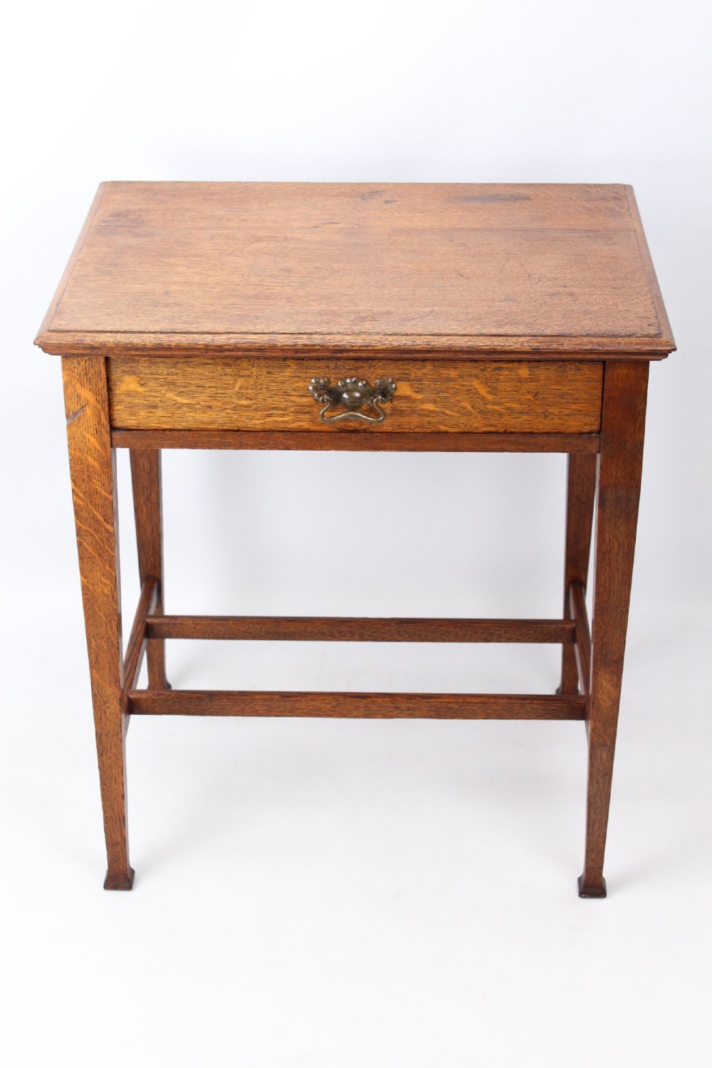 A compact Arts and Crafts oak writing desk featuring a single drawer with a brass drop handle, straight square legs, and lower stretchers.