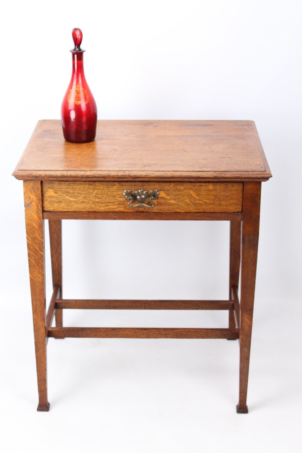 A compact Arts and Crafts oak writing desk featuring a single drawer with a brass drop handle, straight square legs, and lower stretchers. View III