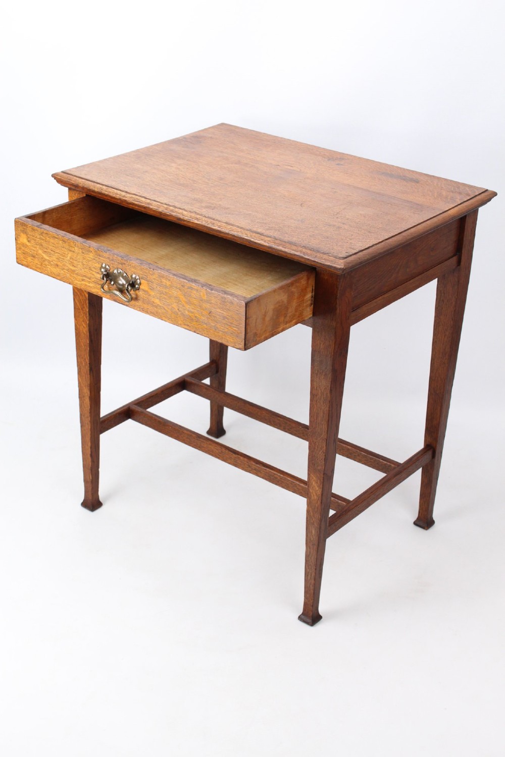 A compact Arts and Crafts oak writing desk featuring a single drawer with a brass drop handle, straight square legs, and lower stretchers. View IV