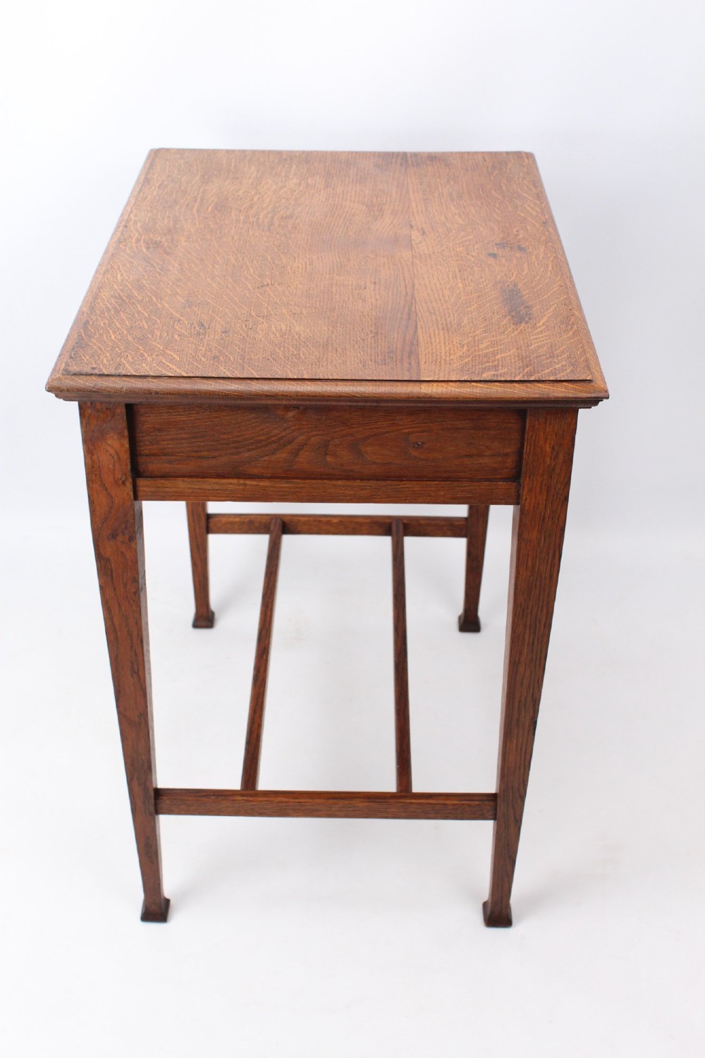A compact Arts and Crafts oak writing desk featuring a single drawer with a brass drop handle, straight square legs, and lower stretchers. View V