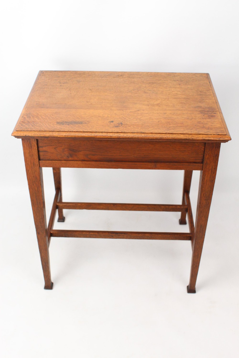A compact Arts and Crafts oak writing desk featuring a single drawer with a brass drop handle, straight square legs, and lower stretchers. View VI