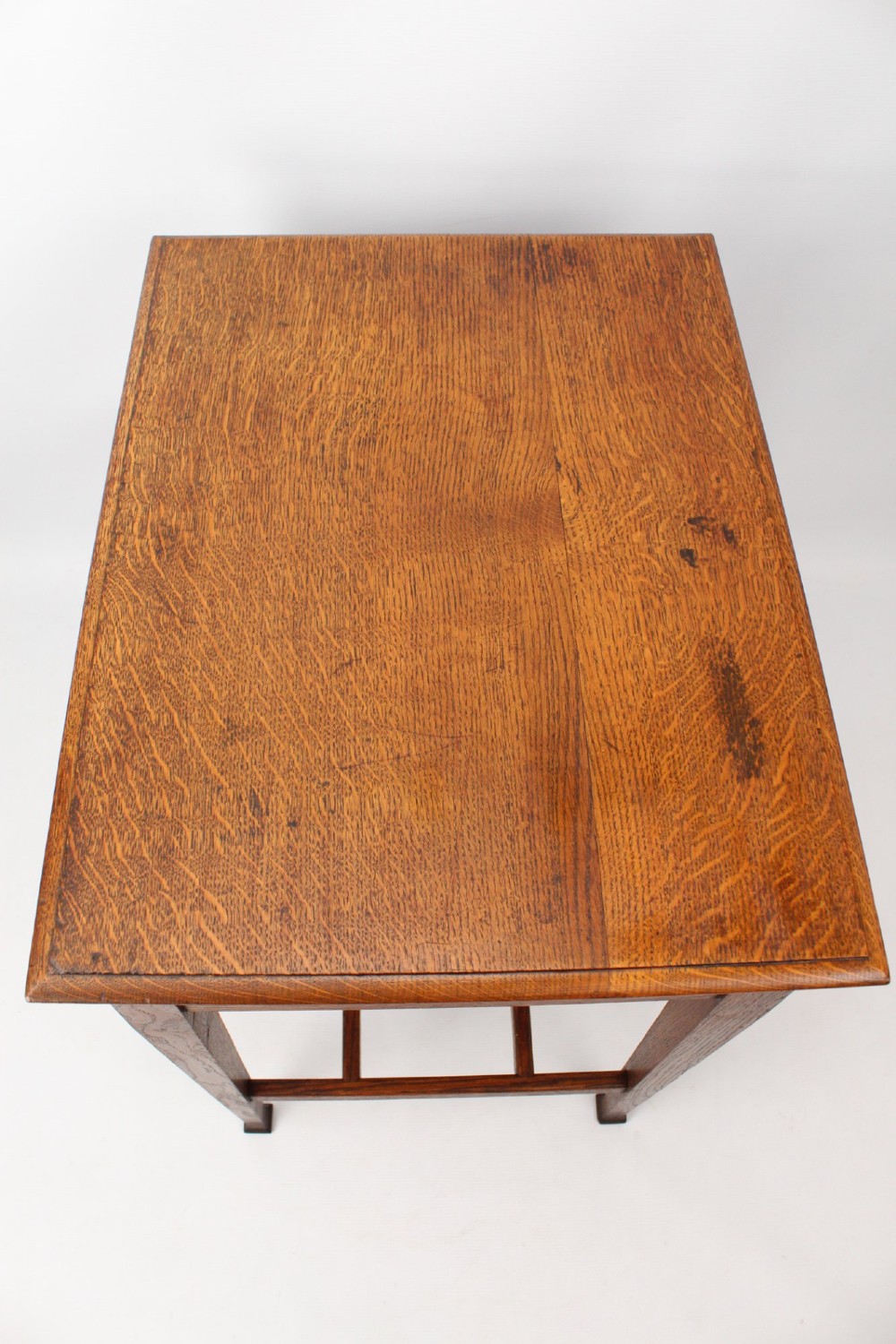A compact Arts and Crafts oak writing desk featuring a single drawer with a brass drop handle, straight square legs, and lower stretchers. View VII