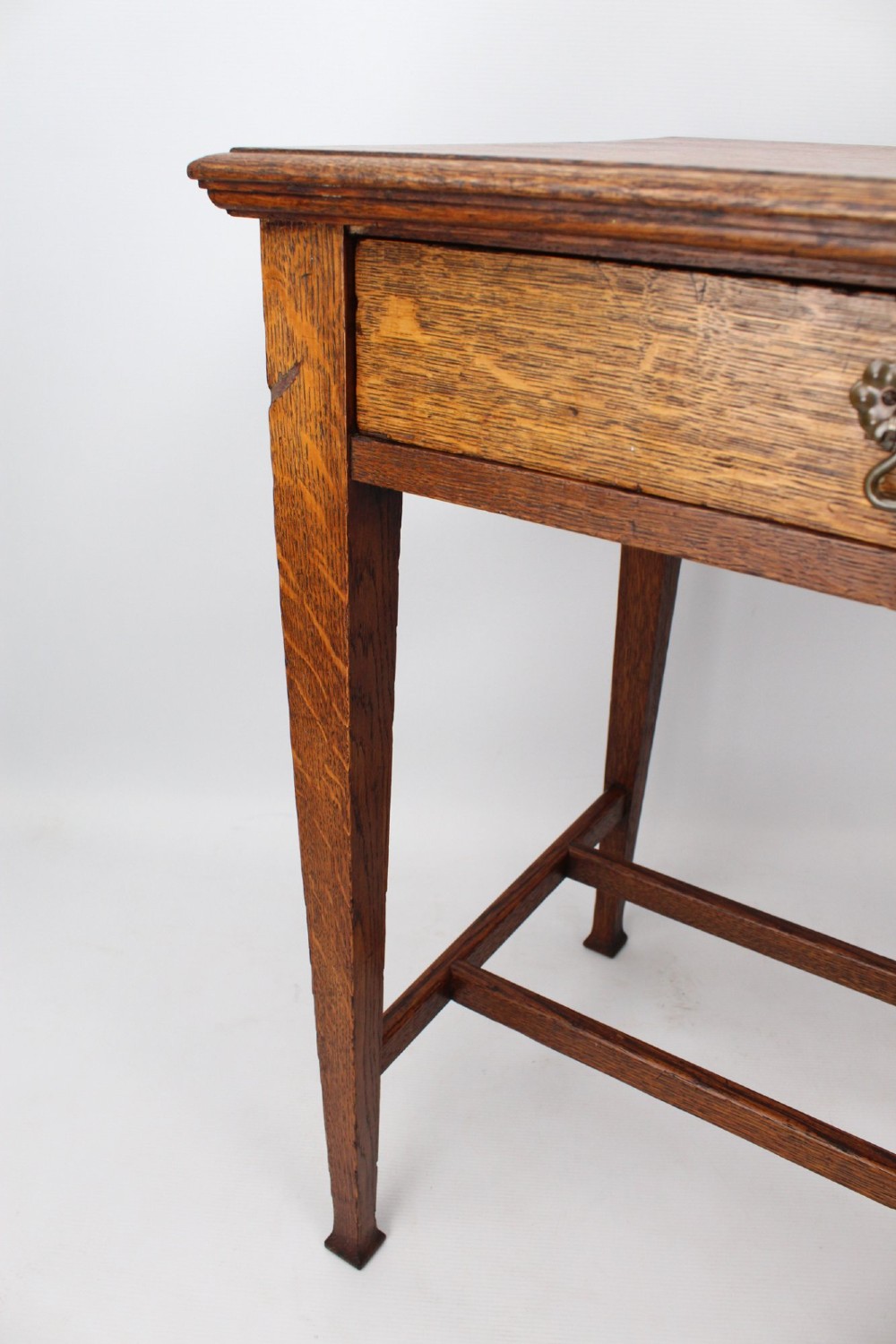 A compact Arts and Crafts oak writing desk featuring a single drawer with a brass drop handle, straight square legs, and lower stretchers. View X