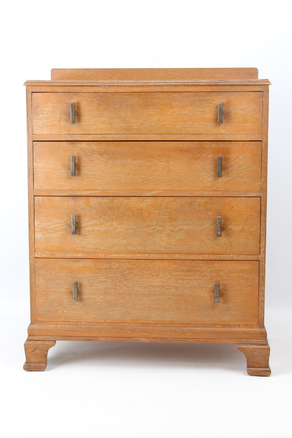 A light oak Art Deco chest of drawers featuring four drawers with textured metal handles, a low gallery back, and bracket feet.