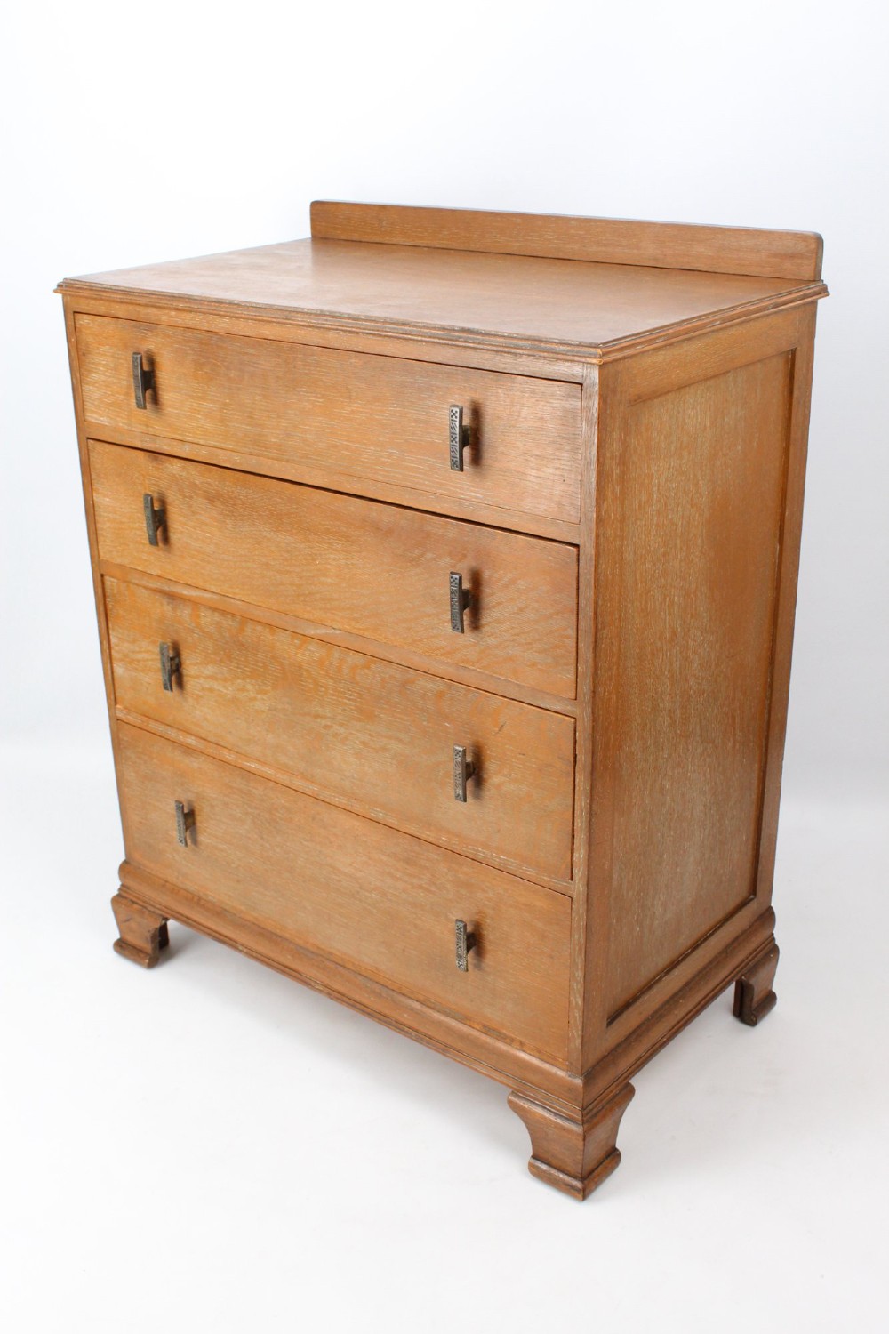 A light oak Art Deco chest of drawers featuring four drawers with textured metal handles, a low gallery back, and bracket feet. View III