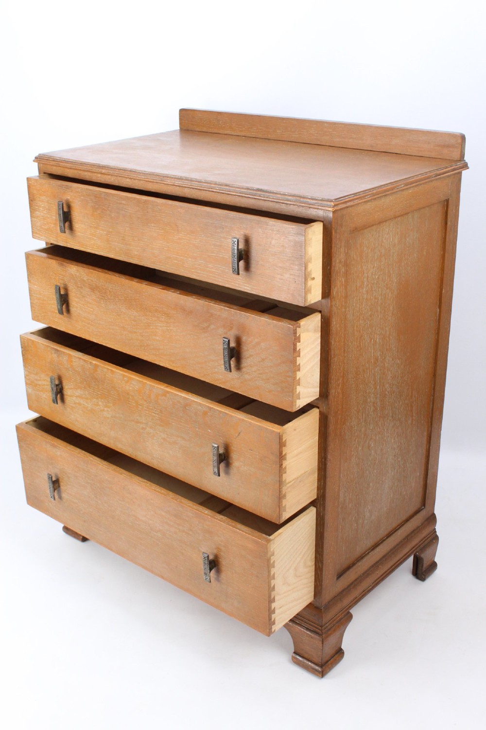 A light oak Art Deco chest of drawers featuring four drawers with textured metal handles, a low gallery back, and bracket feet. View IV