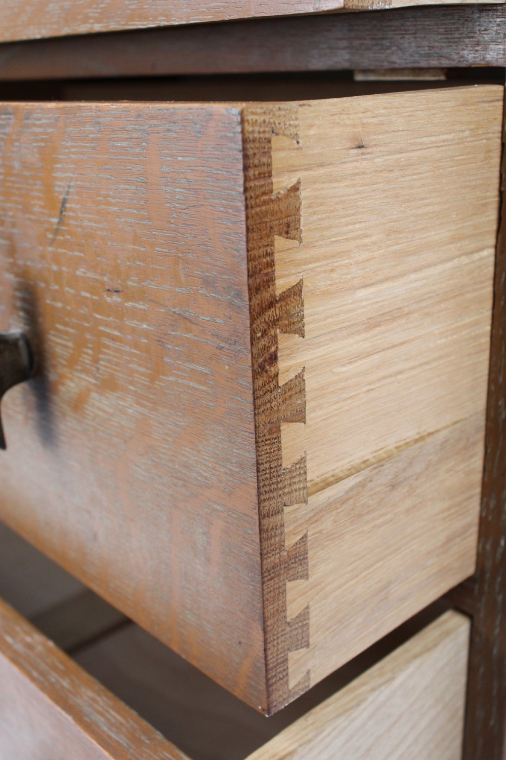 A light oak Art Deco chest of drawers featuring four drawers with textured metal handles, a low gallery back, and bracket feet. View VII