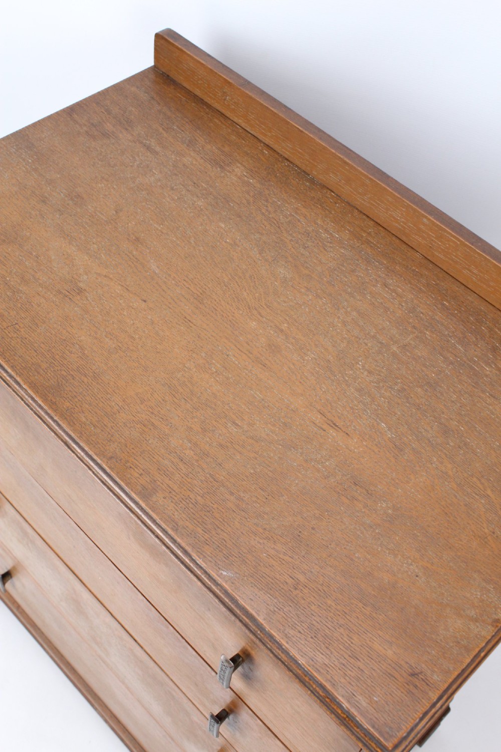 A light oak Art Deco chest of drawers featuring four drawers with textured metal handles, a low gallery back, and bracket feet. View XII
