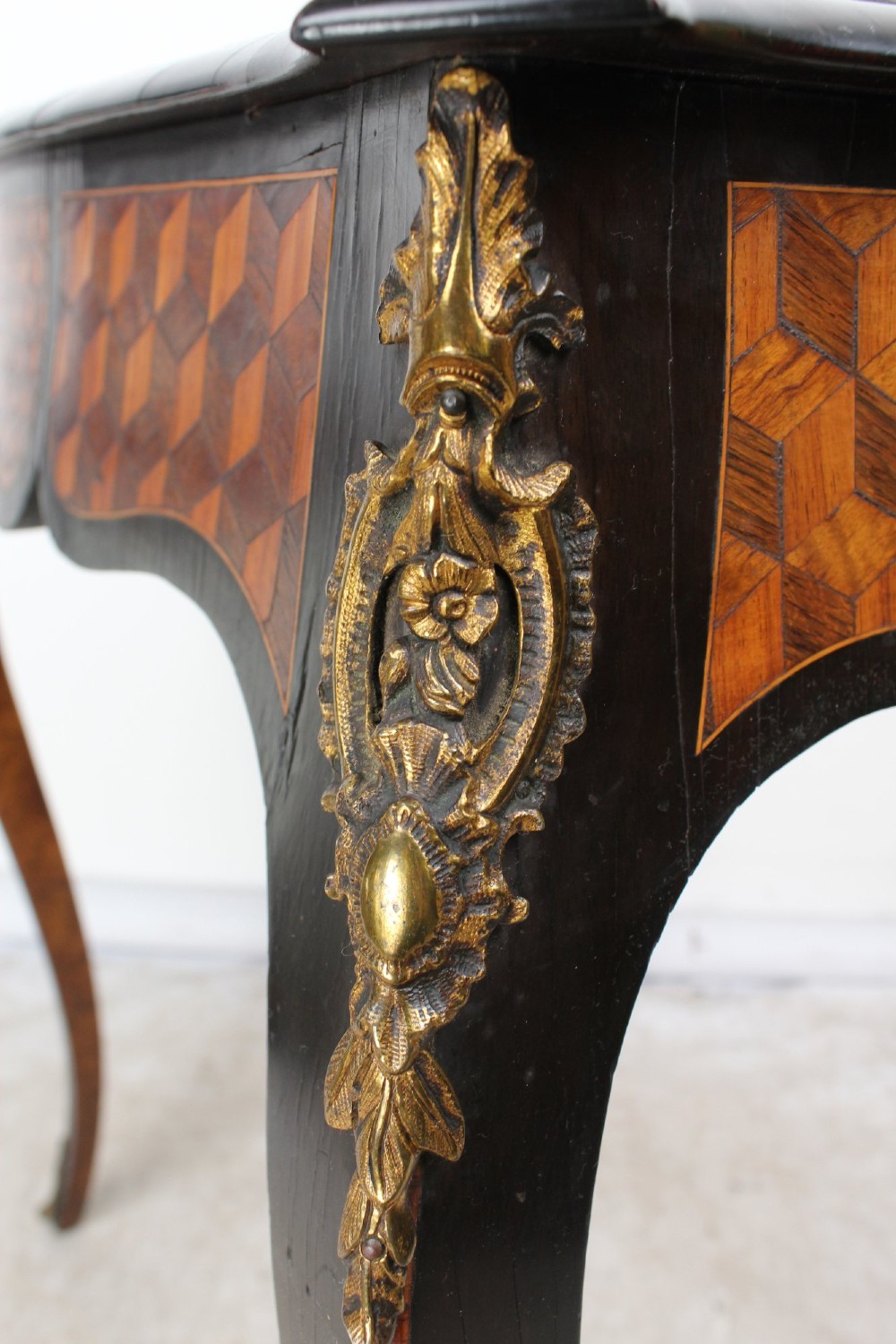 A Victorian Louis XV Revival writing table featuring geometric cube parquetry inlay, serpentine edges, ebonised borders, cabriole legs, and gold-toned bronze mounts. View X