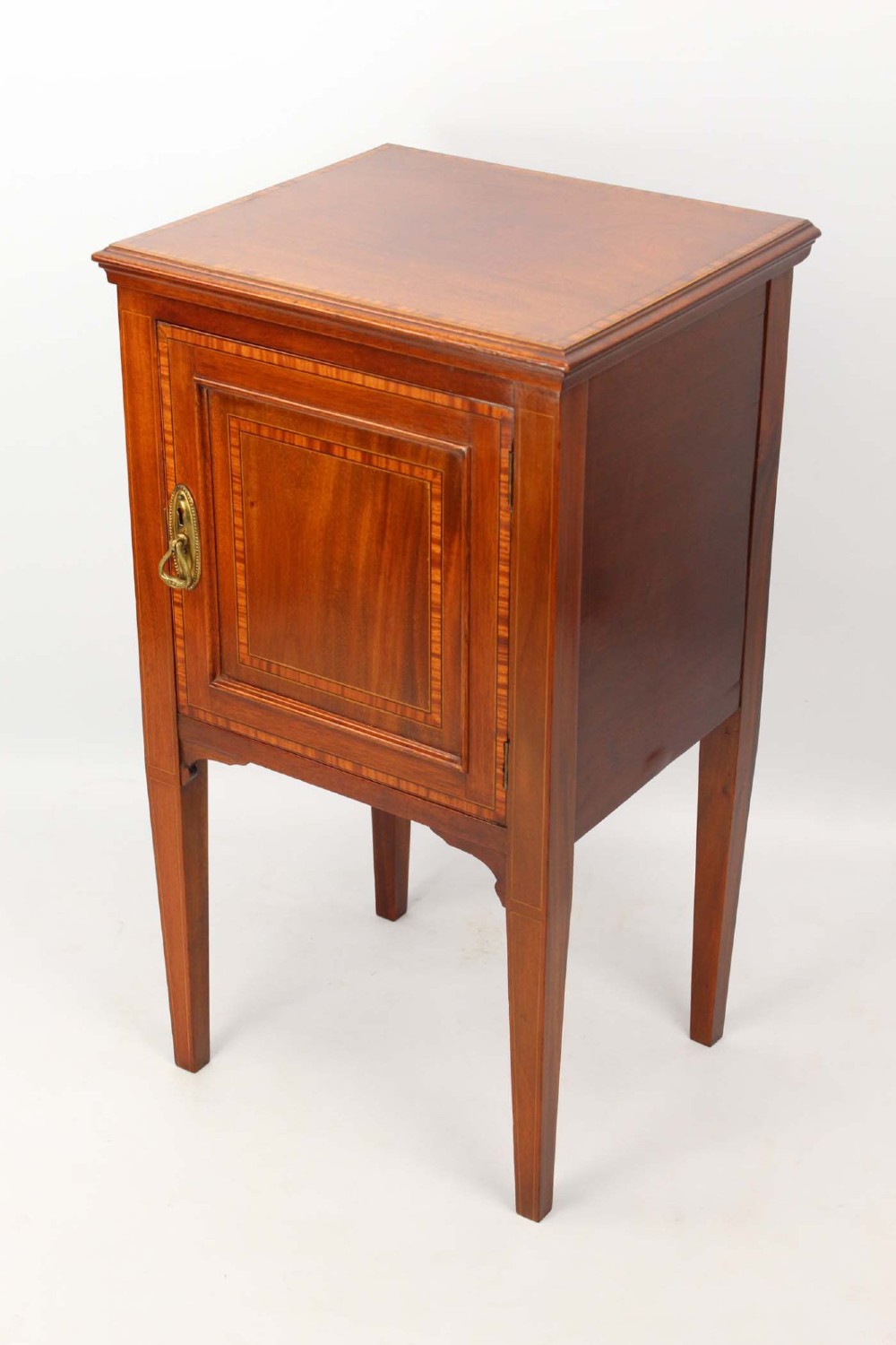 An Edwardian mahogany bedside cabinet featuring satinwood stringing inlay, a single panelled door with a brass handle, and square tapered legs. View III