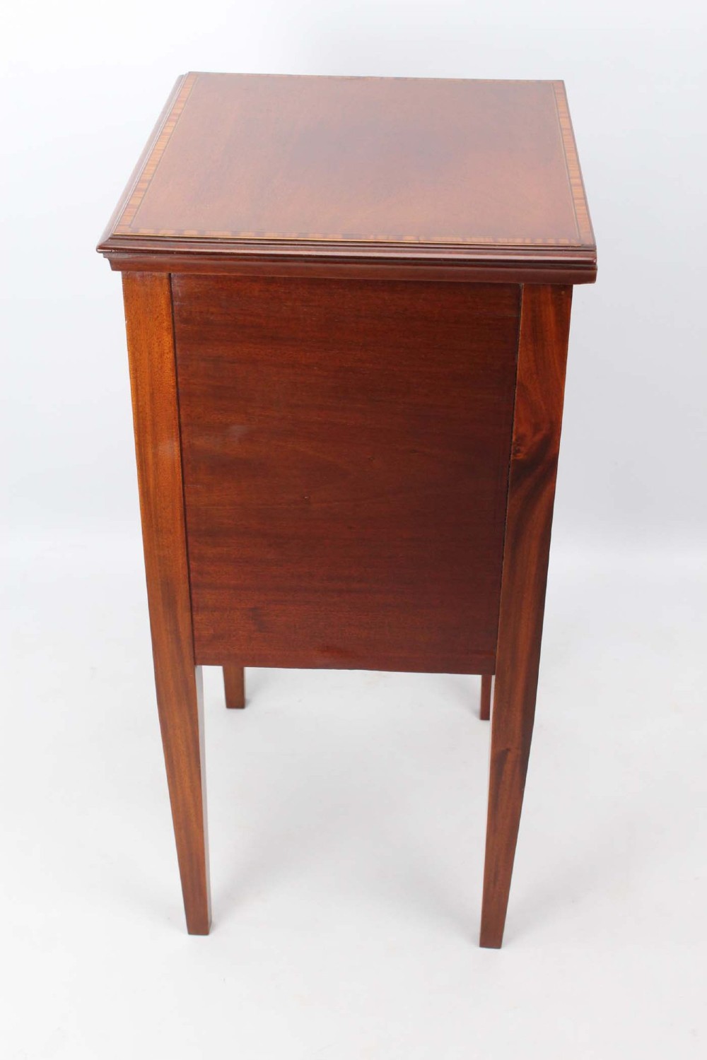 An Edwardian mahogany bedside cabinet featuring satinwood stringing inlay, a single panelled door with a brass handle, and square tapered legs. View IV