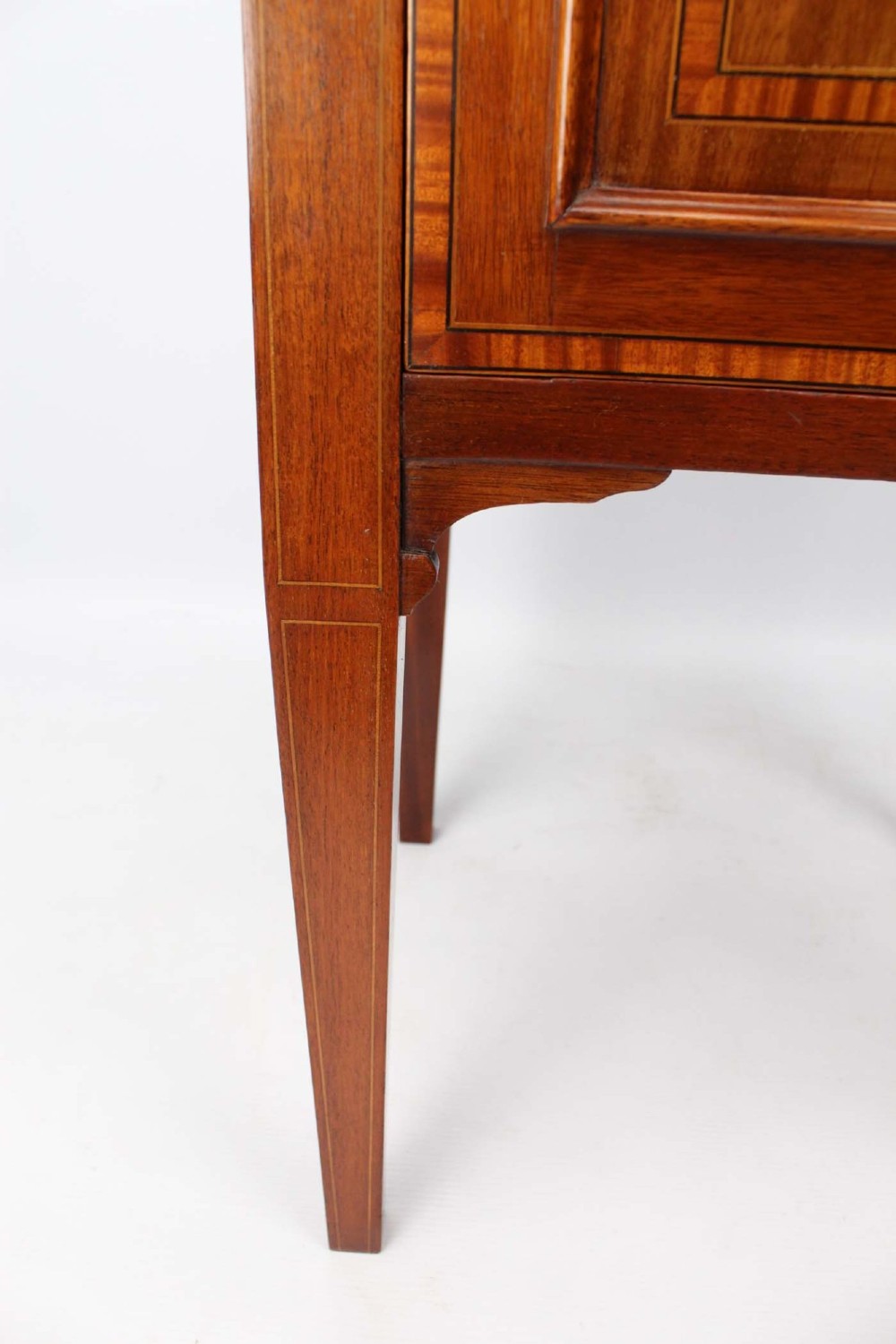 An Edwardian mahogany bedside cabinet featuring satinwood stringing inlay, a single panelled door with a brass handle, and square tapered legs. View XI