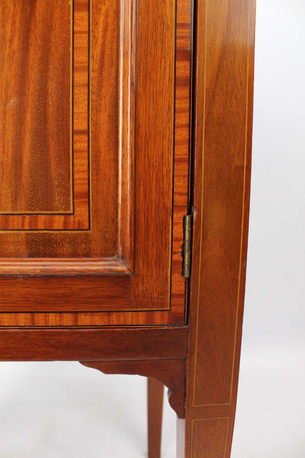 An Edwardian mahogany bedside cabinet featuring satinwood stringing inlay, a single panelled door with a brass handle, and square tapered legs. View XII