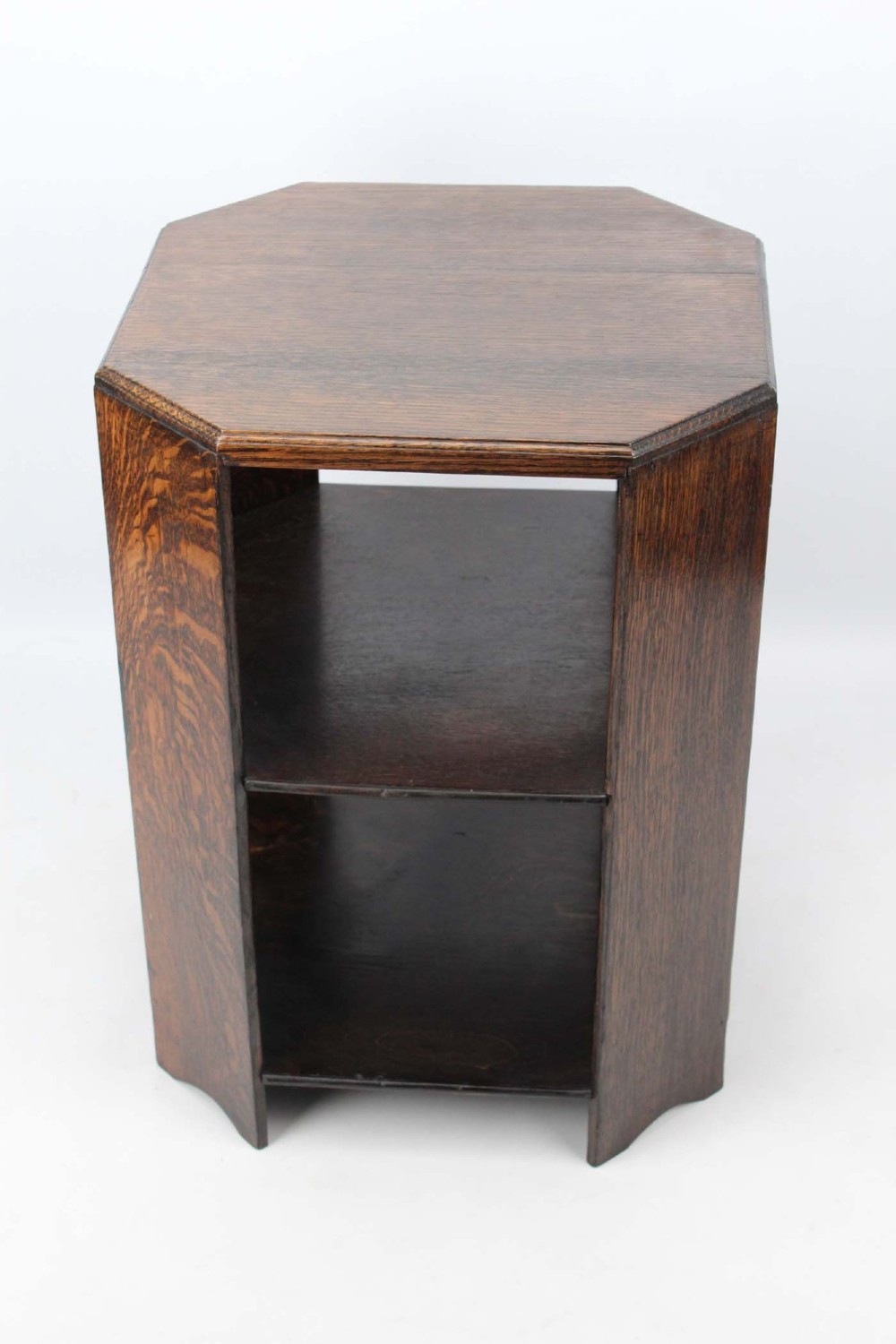 An octagonal dark oak Art Deco style book table featuring three vertical side panels and two open lower shelves. View II