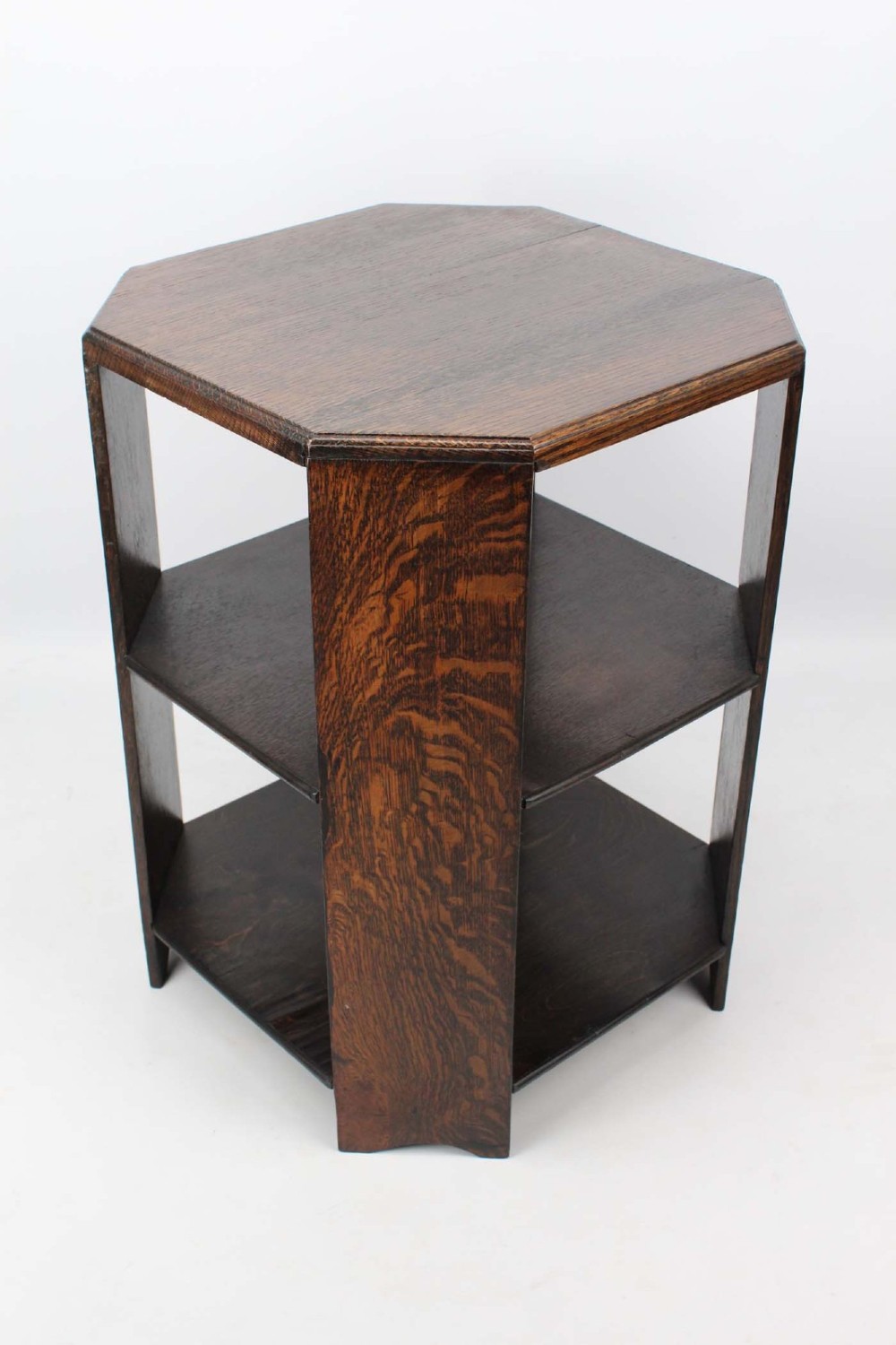 An octagonal dark oak Art Deco style book table featuring three vertical side panels and two open lower shelves. View III