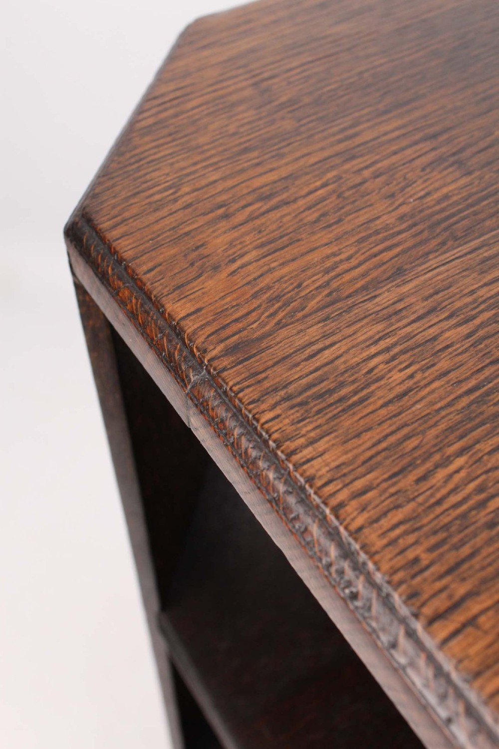 An octagonal dark oak Art Deco style book table featuring three vertical side panels and two open lower shelves. View IX