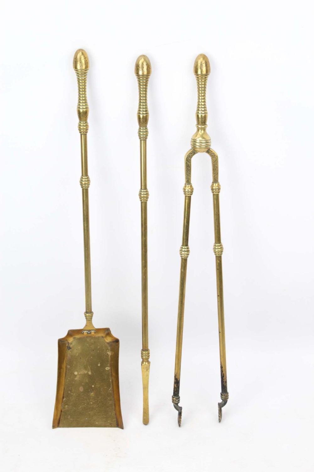 A three-piece set of Victorian brass fire tools consisting of a shovel, a poker, and tongs with turned and engraved handles.