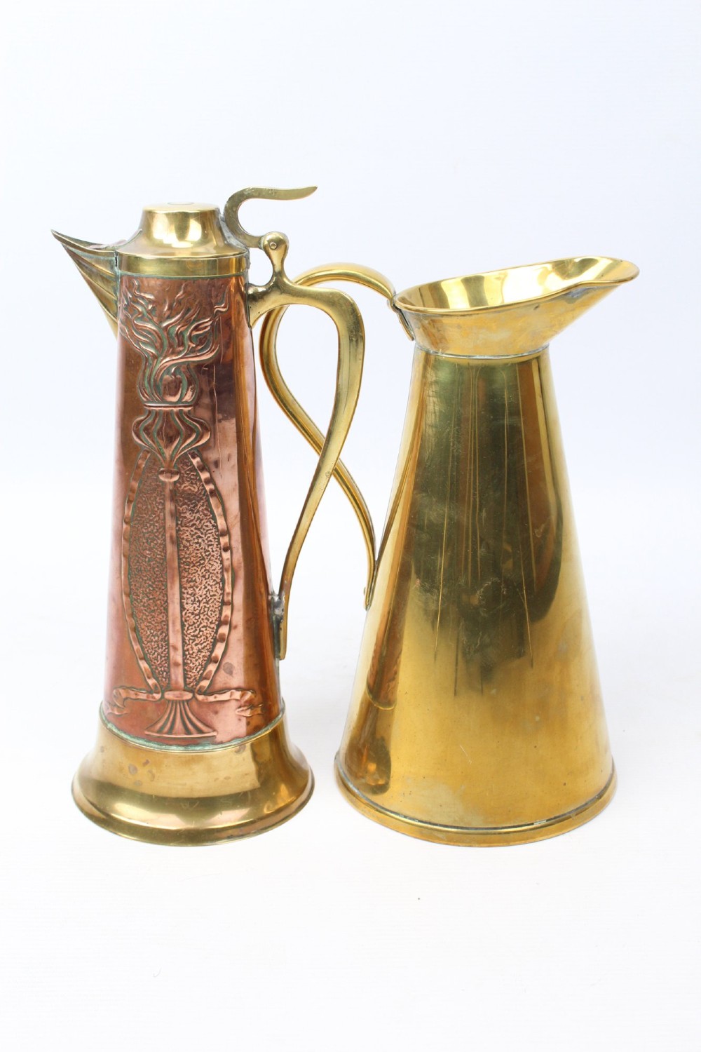 A pair of antique metal jugs, one crafted from repousse copper with brass fittings and a hinged lid alongside a tapered solid brass pitcher.