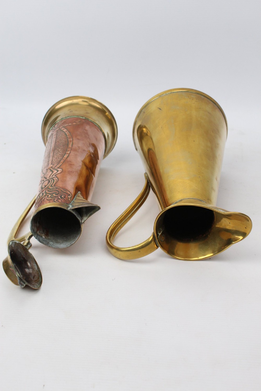 A pair of antique metal jugs, one crafted from repousse copper with brass fittings and a hinged lid alongside a tapered solid brass pitcher. View IV