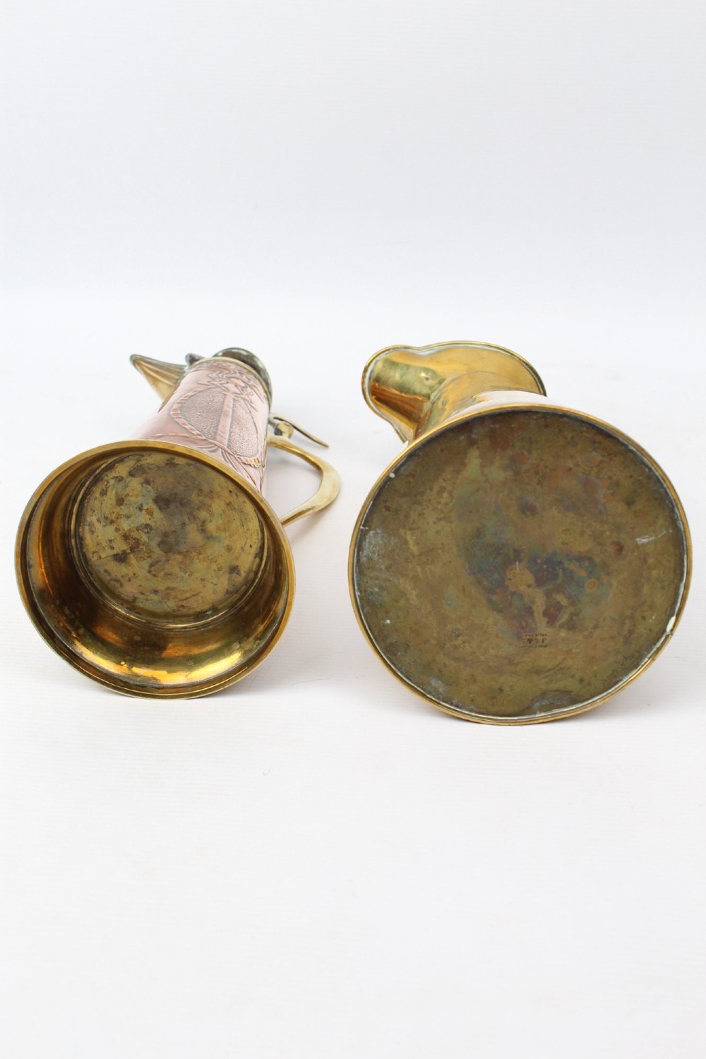A pair of antique metal jugs, one crafted from repousse copper with brass fittings and a hinged lid alongside a tapered solid brass pitcher. View V