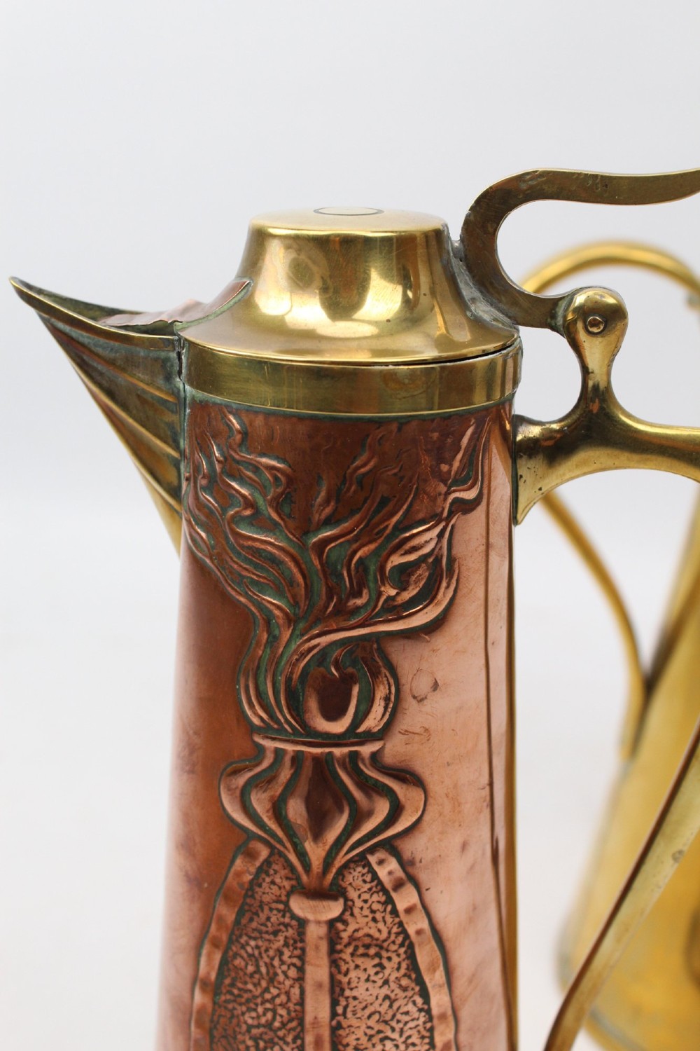 A pair of antique metal jugs, one crafted from repousse copper with brass fittings and a hinged lid alongside a tapered solid brass pitcher. View VII