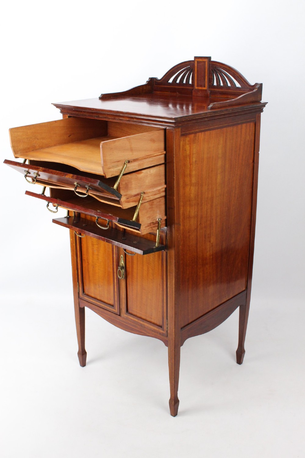 An Edwardian mahogany music cabinet featuring inlaid stringing, three top drawers with brass handles, a two-door lower cupboard, and a carved cresting gallery. View III