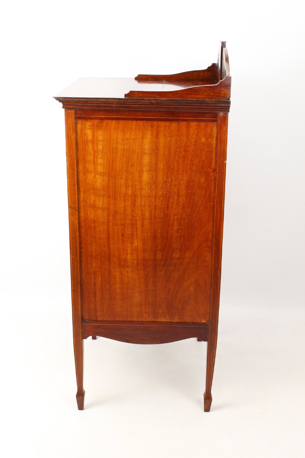 An Edwardian mahogany music cabinet featuring inlaid stringing, three top drawers with brass handles, a two-door lower cupboard, and a carved cresting gallery. View IV