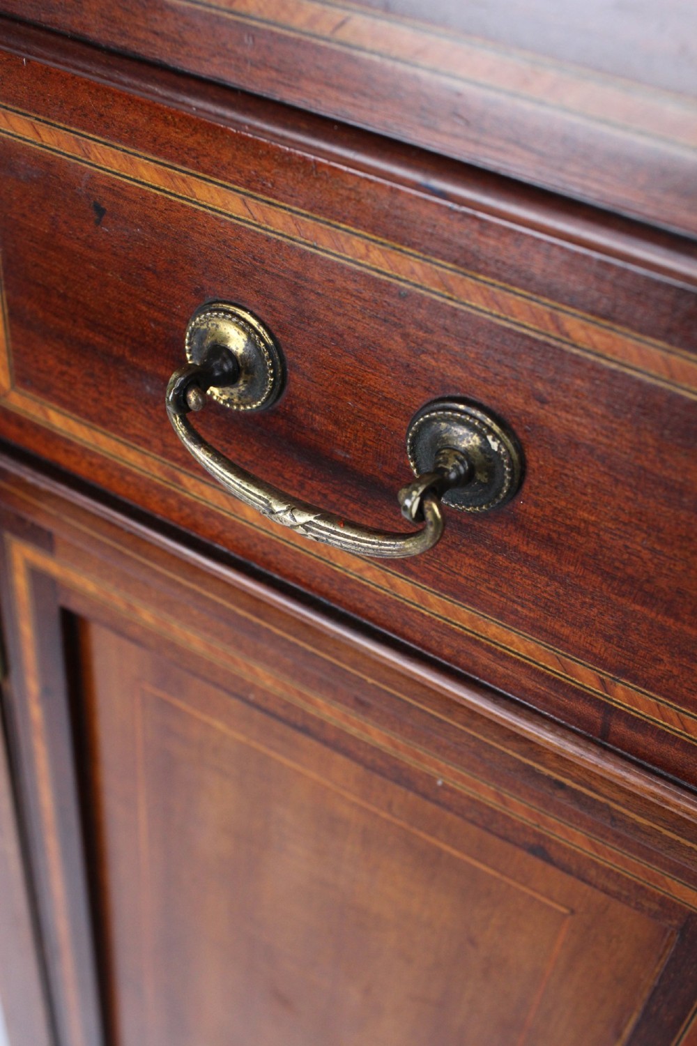An Edwardian mahogany music cabinet featuring inlaid stringing, three top drawers with brass handles, a two-door lower cupboard, and a carved cresting gallery. View VII