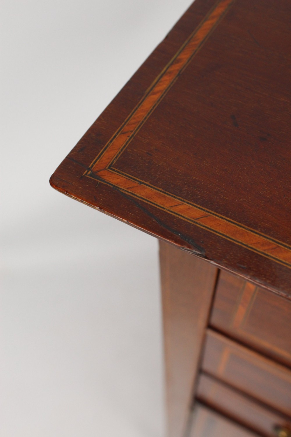 An Edwardian mahogany music cabinet featuring inlaid stringing, three top drawers with brass handles, a two-door lower cupboard, and a carved cresting gallery. View VIII