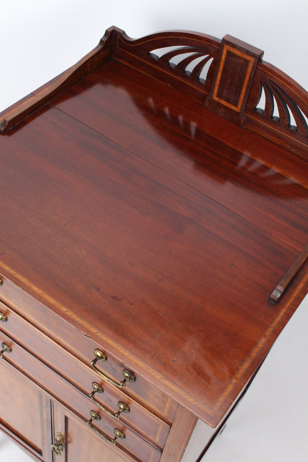 An Edwardian mahogany music cabinet featuring inlaid stringing, three top drawers with brass handles, a two-door lower cupboard, and a carved cresting gallery. View IX