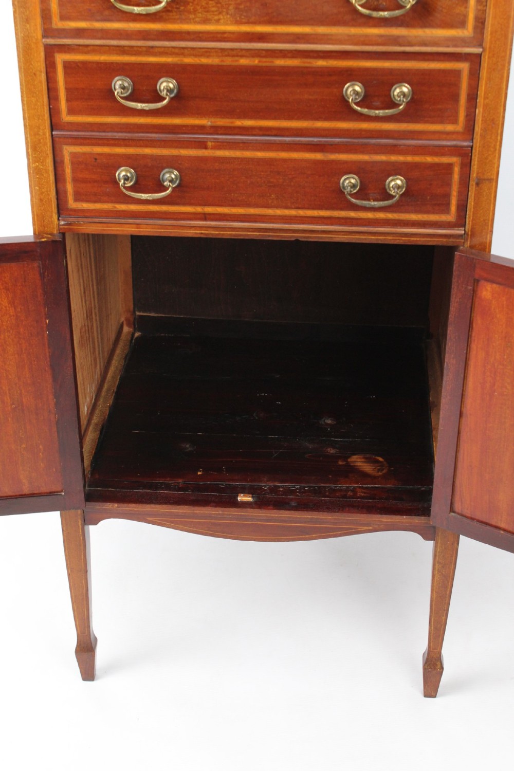 An Edwardian mahogany music cabinet featuring inlaid stringing, three top drawers with brass handles, a two-door lower cupboard, and a carved cresting gallery. View XI
