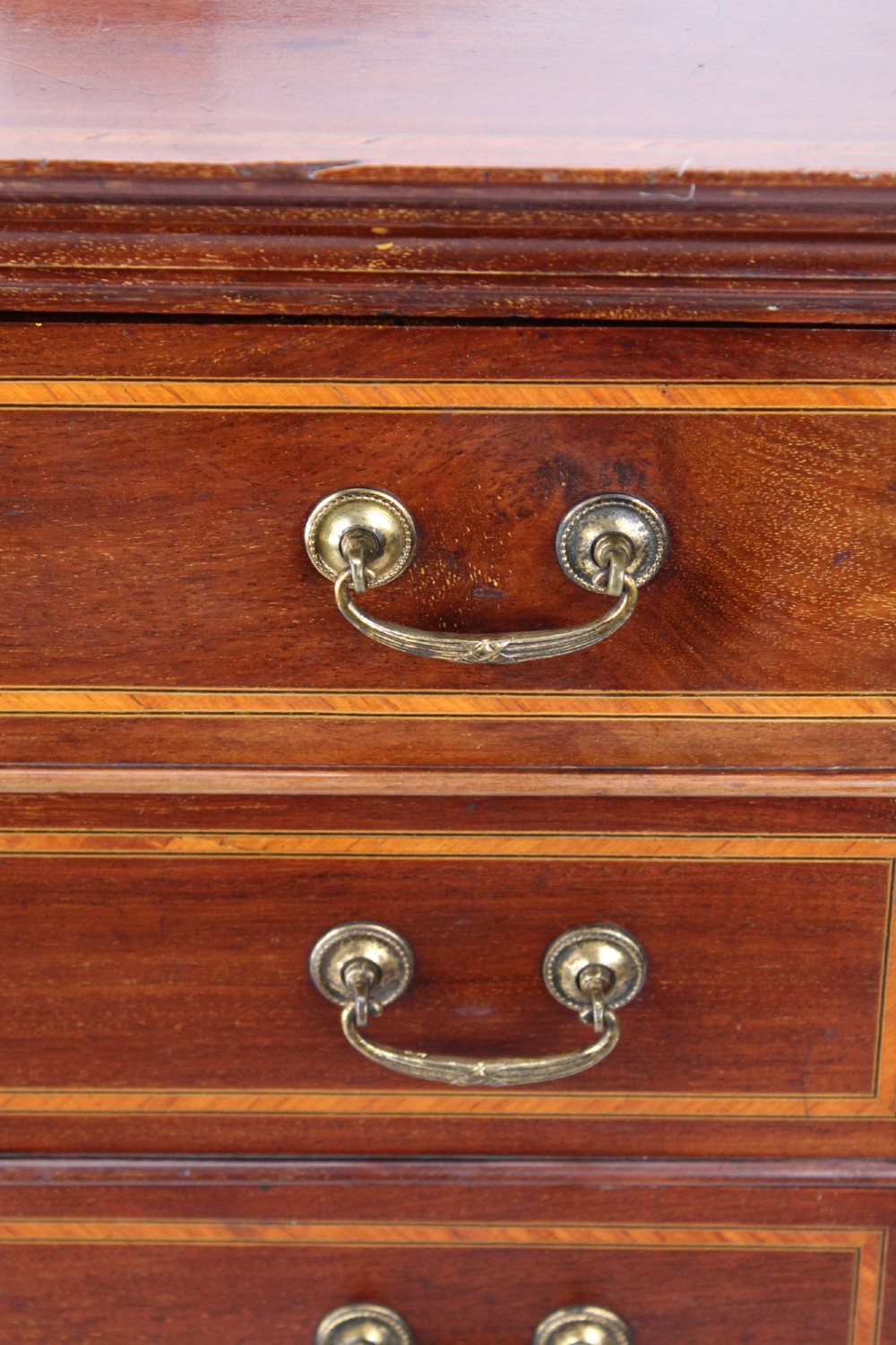 An Edwardian mahogany music cabinet featuring inlaid stringing, three top drawers with brass handles, a two-door lower cupboard, and a carved cresting gallery. View XIII