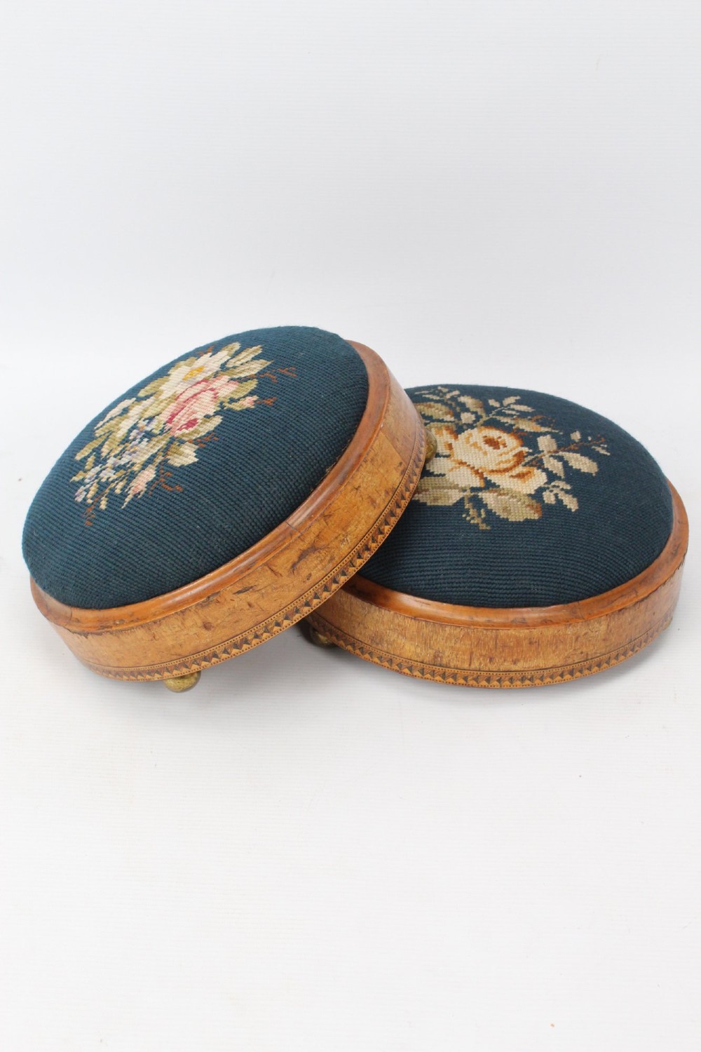 A pair of circular Early Victorian footstools featuring teal floral needlepoint tops within light wood frames and geometric mosaic borders. View II