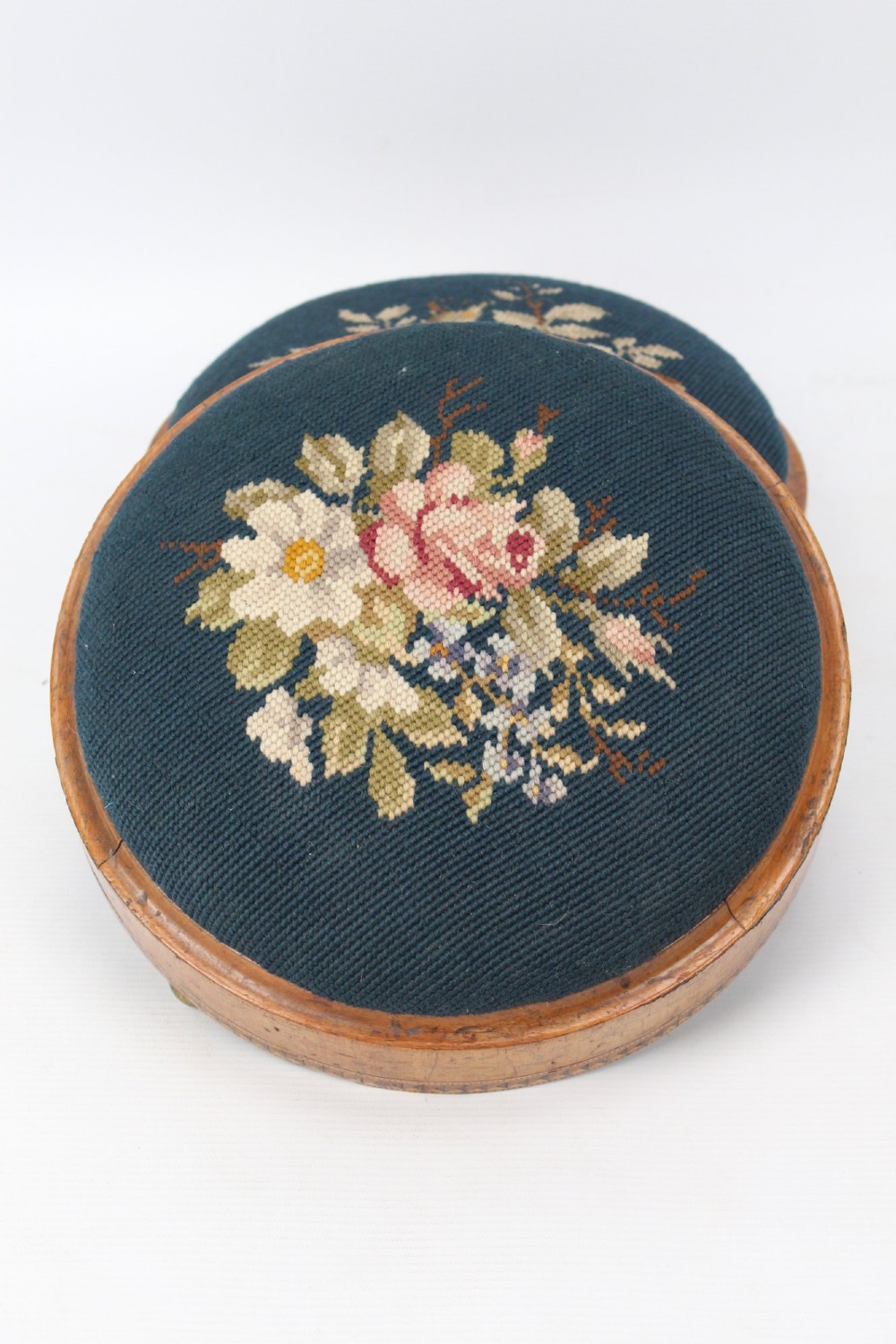 A pair of circular Early Victorian footstools featuring teal floral needlepoint tops within light wood frames and geometric mosaic borders. View III
