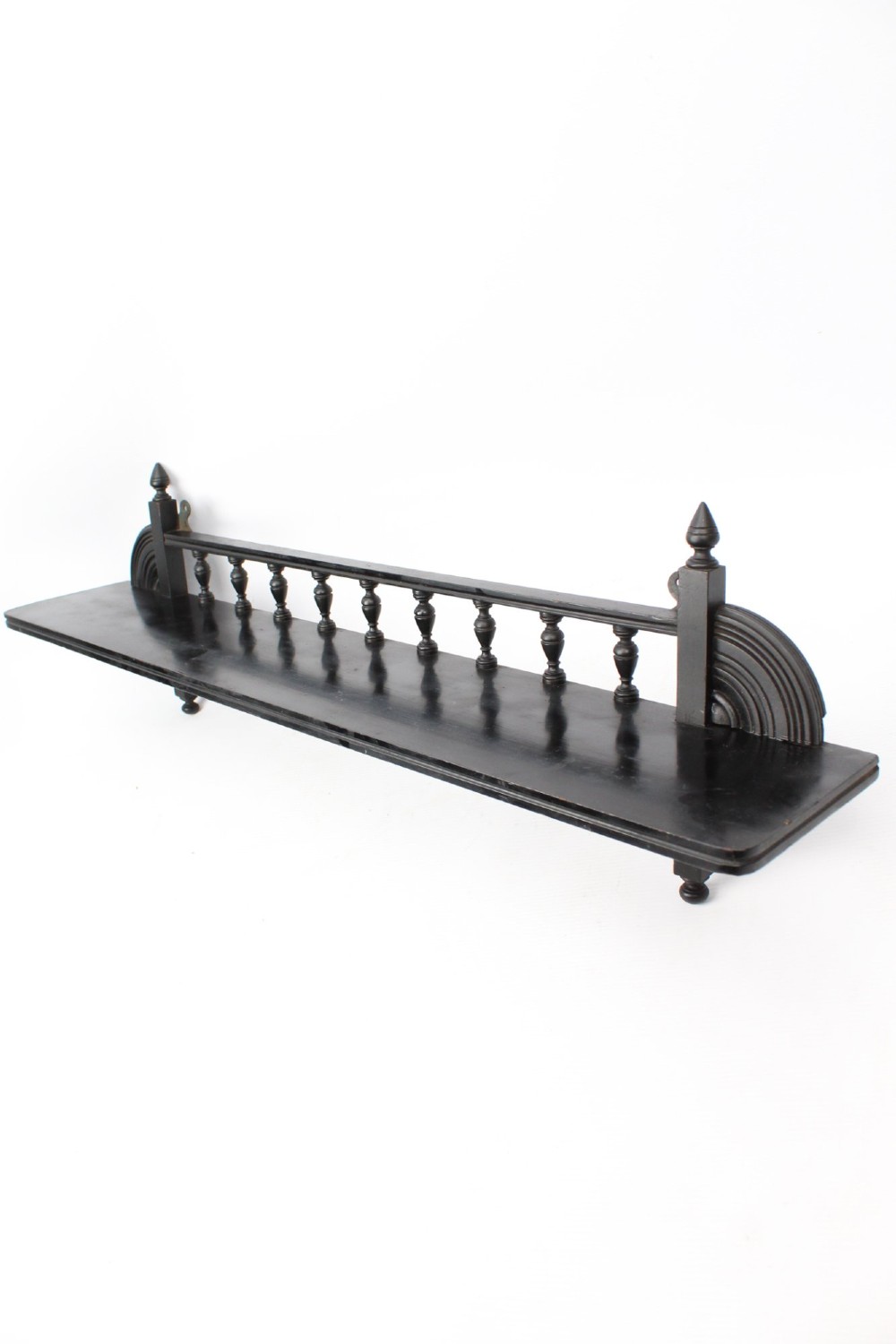 An ebonised wooden hanging wall shelf featuring a low spindle balustrade rail, turned finials, and decorative corner mouldings.