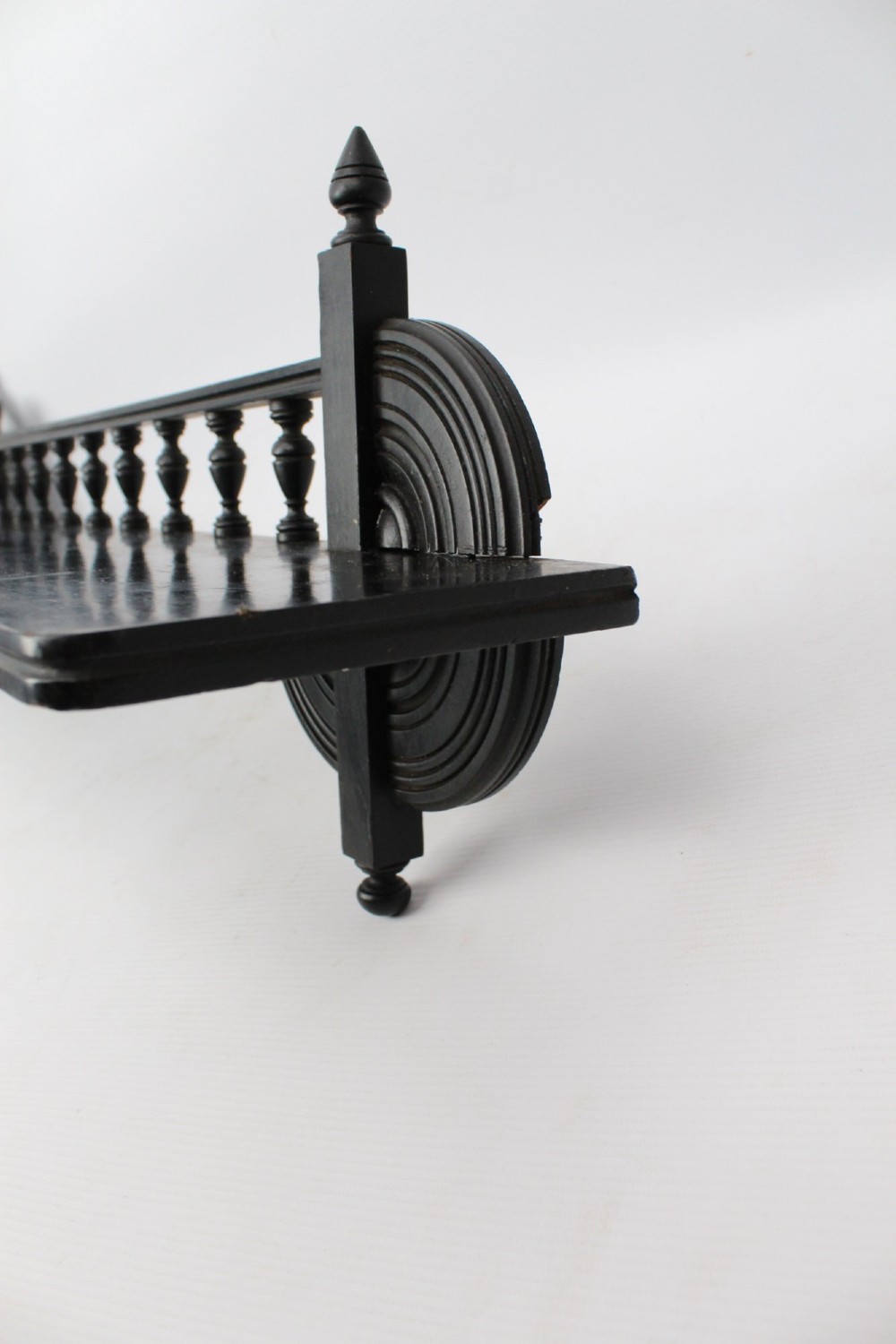An ebonised wooden hanging wall shelf featuring a low spindle balustrade rail, turned finials, and decorative corner mouldings. View XIII