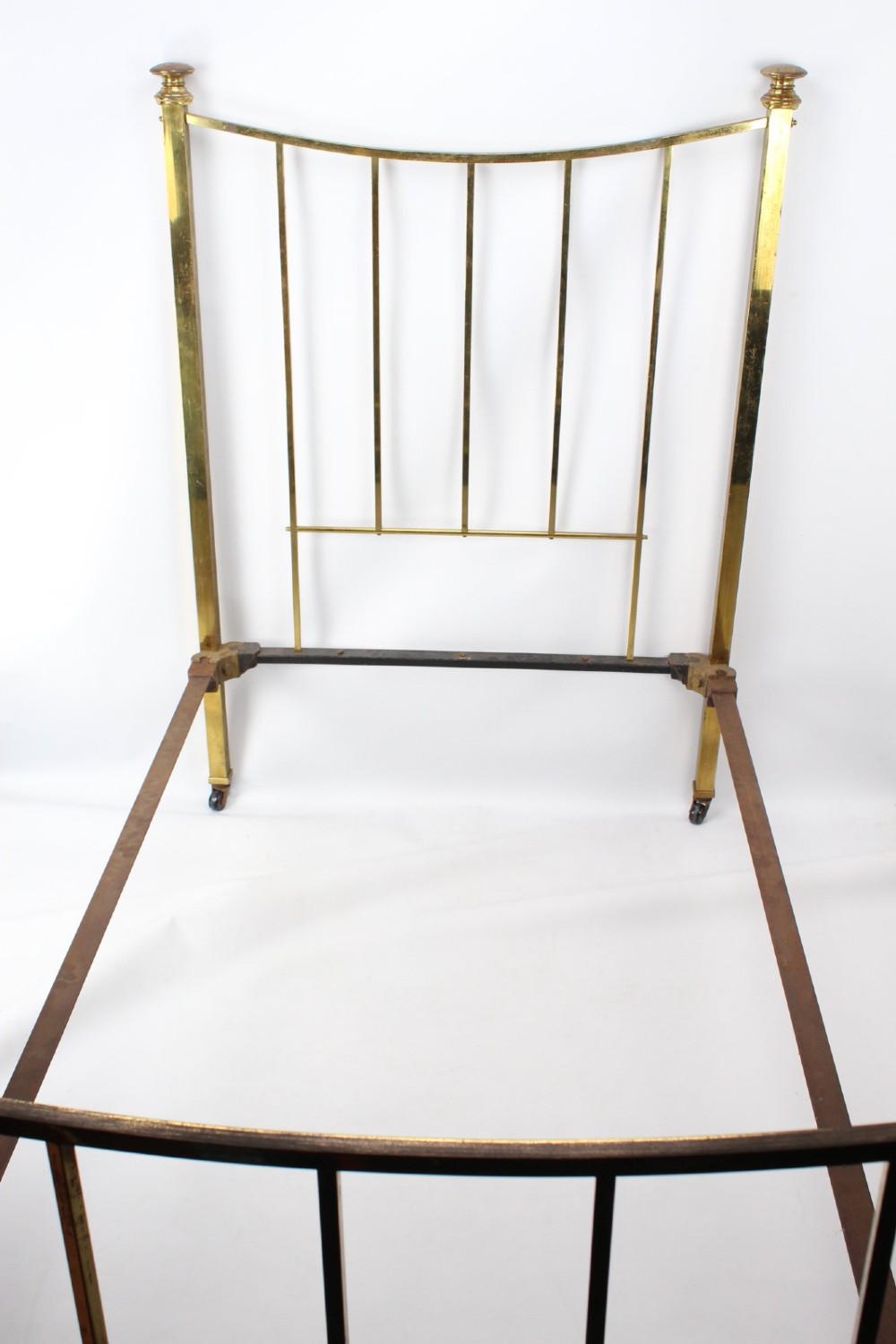 A Victorian brass single bed frame featuring a gently curved top rail, vertical spindles, turned finials, and original wheel castors. View IV