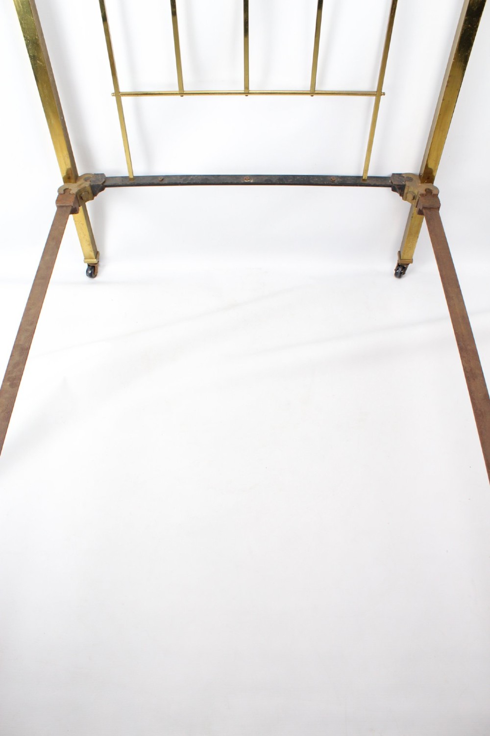A Victorian brass single bed frame featuring a gently curved top rail, vertical spindles, turned finials, and original wheel castors. View V