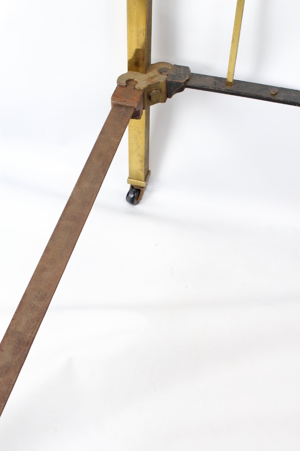 A Victorian brass single bed frame featuring a gently curved top rail, vertical spindles, turned finials, and original wheel castors. View VI