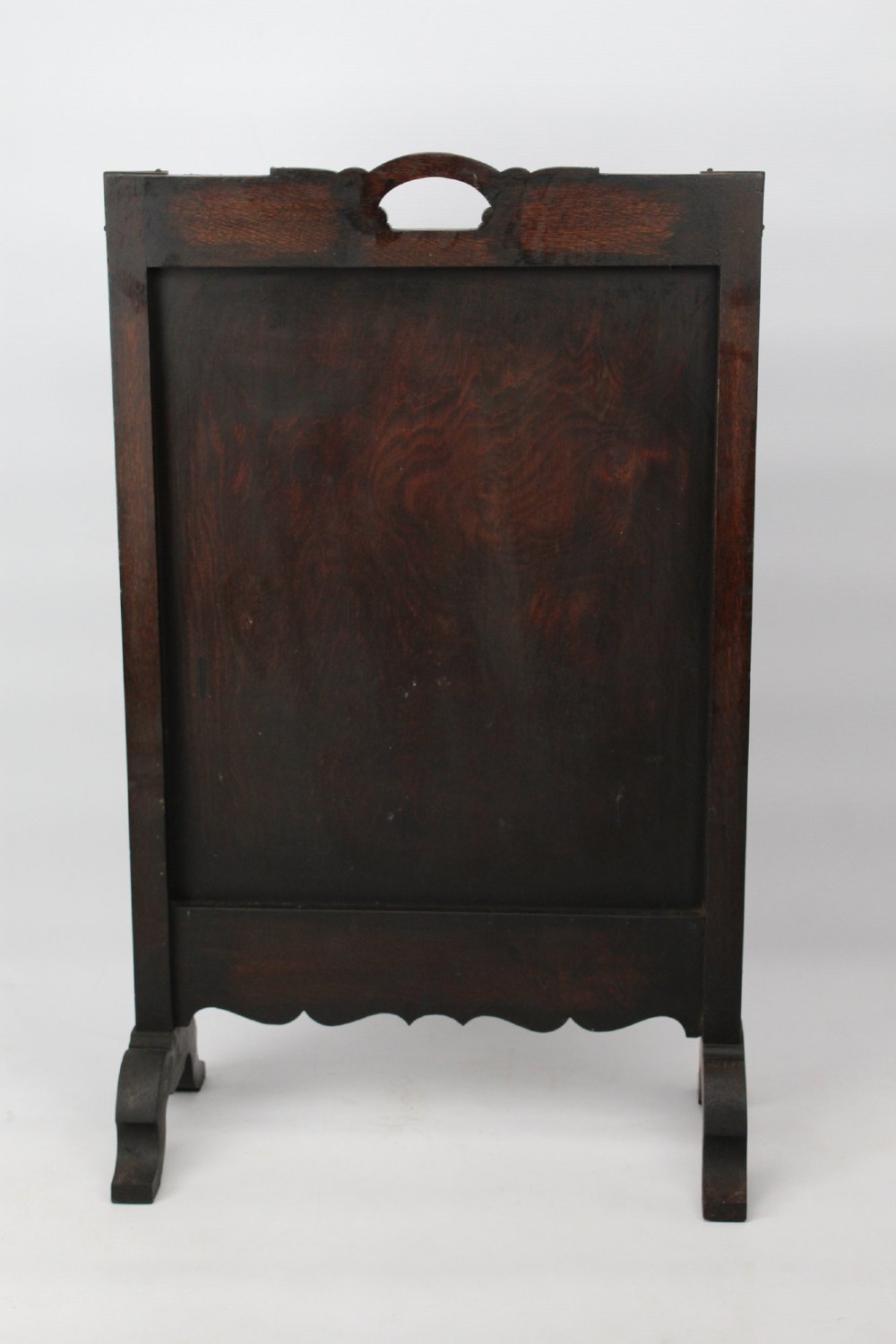 An Edwardian Arts and Crafts fire screen constructed from carved oak and warm brown leather featuring brass studwork and a central oval motif. View IV