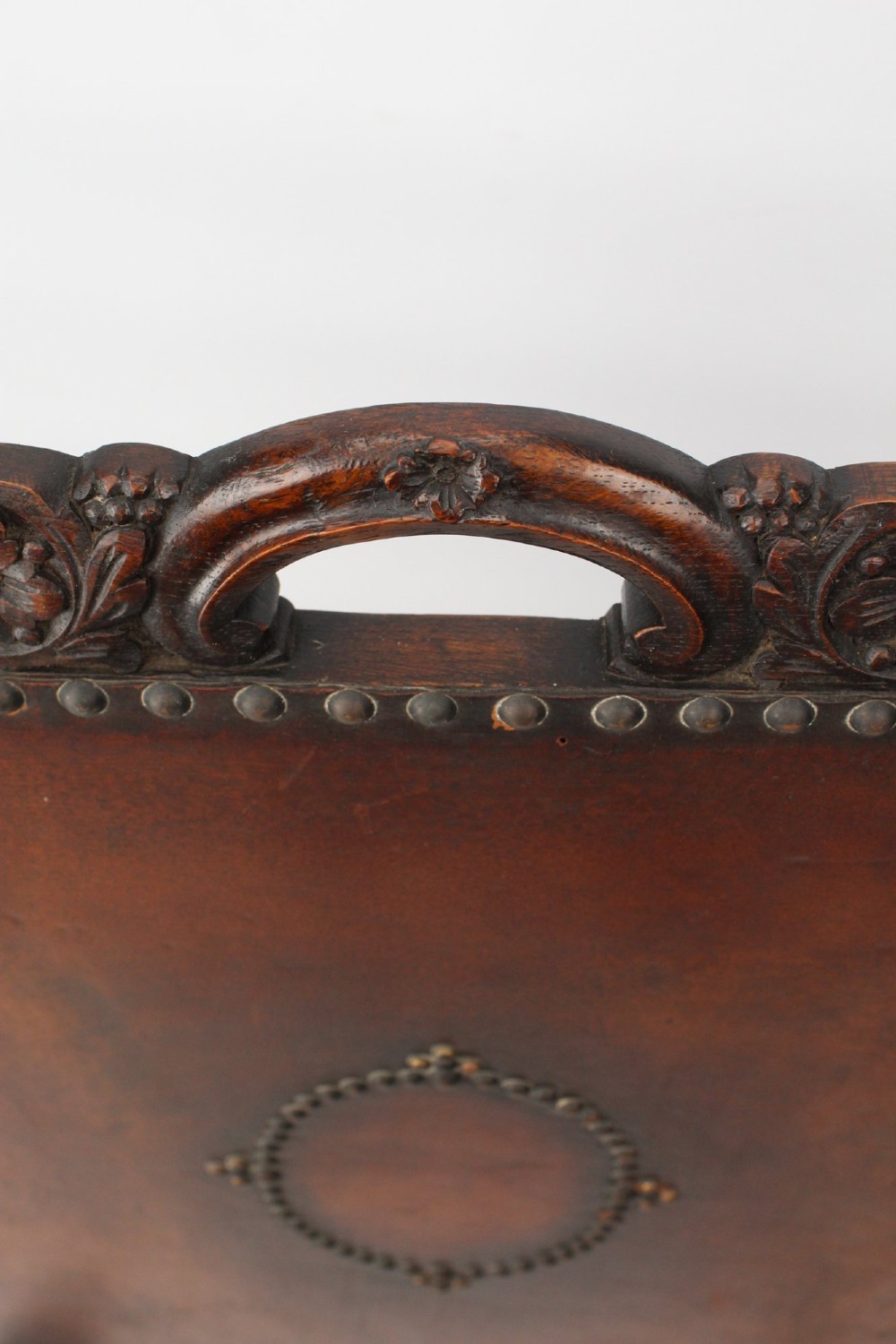 An Edwardian Arts and Crafts fire screen constructed from carved oak and warm brown leather featuring brass studwork and a central oval motif. View X