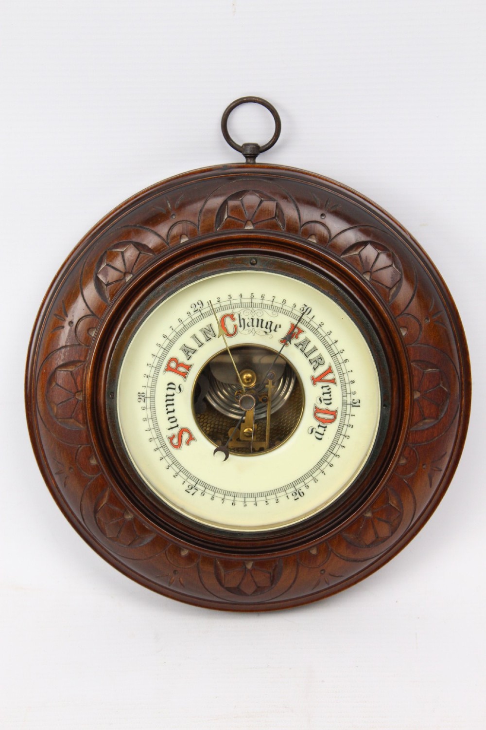 A circular Victorian walnut wall barometer featuring a carved wooden border, a brass hanging ring, and an exposed brass skeleton movement within an enamel dial. View II