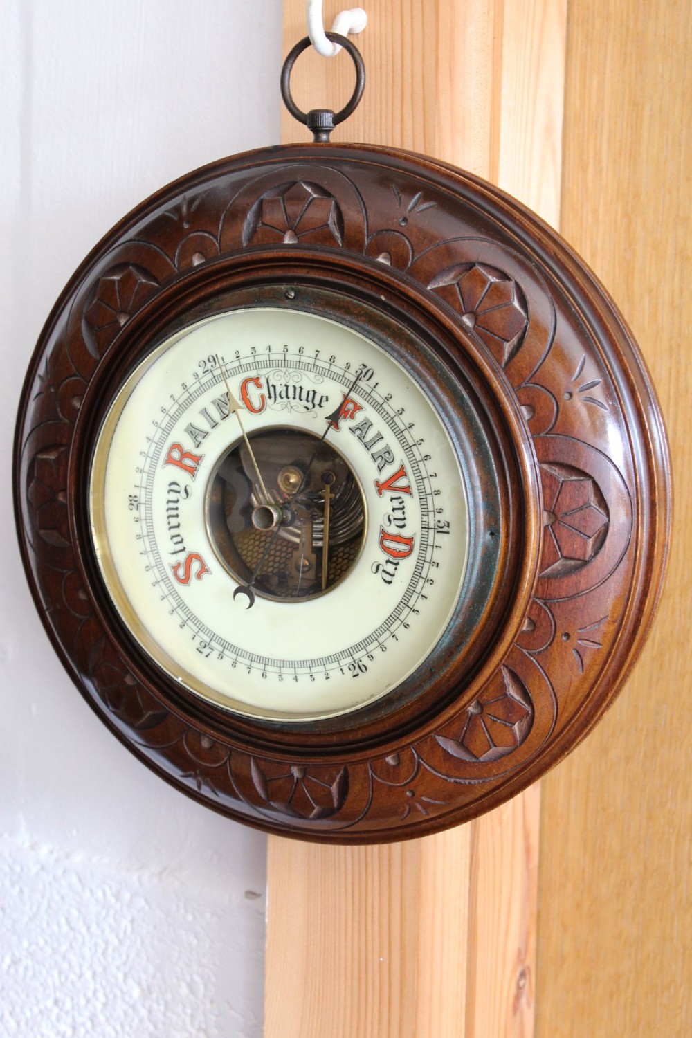 A circular Victorian walnut wall barometer featuring a carved wooden border, a brass hanging ring, and an exposed brass skeleton movement within an enamel dial. View III