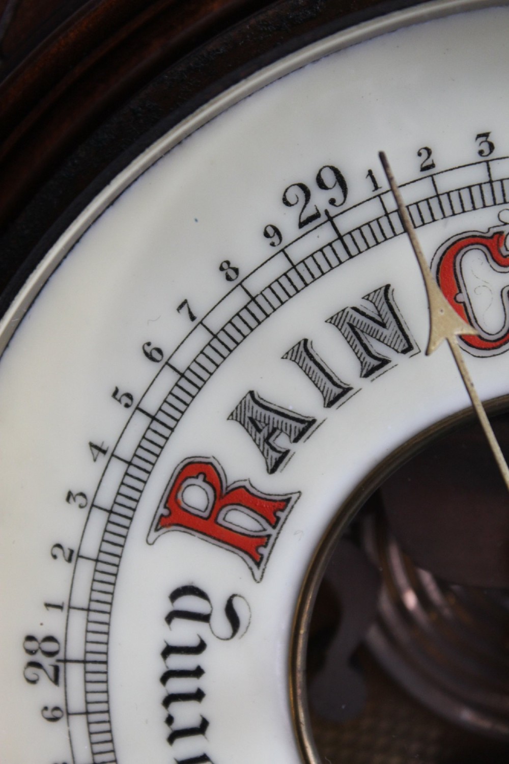 A circular Victorian walnut wall barometer featuring a carved wooden border, a brass hanging ring, and an exposed brass skeleton movement within an enamel dial. View V