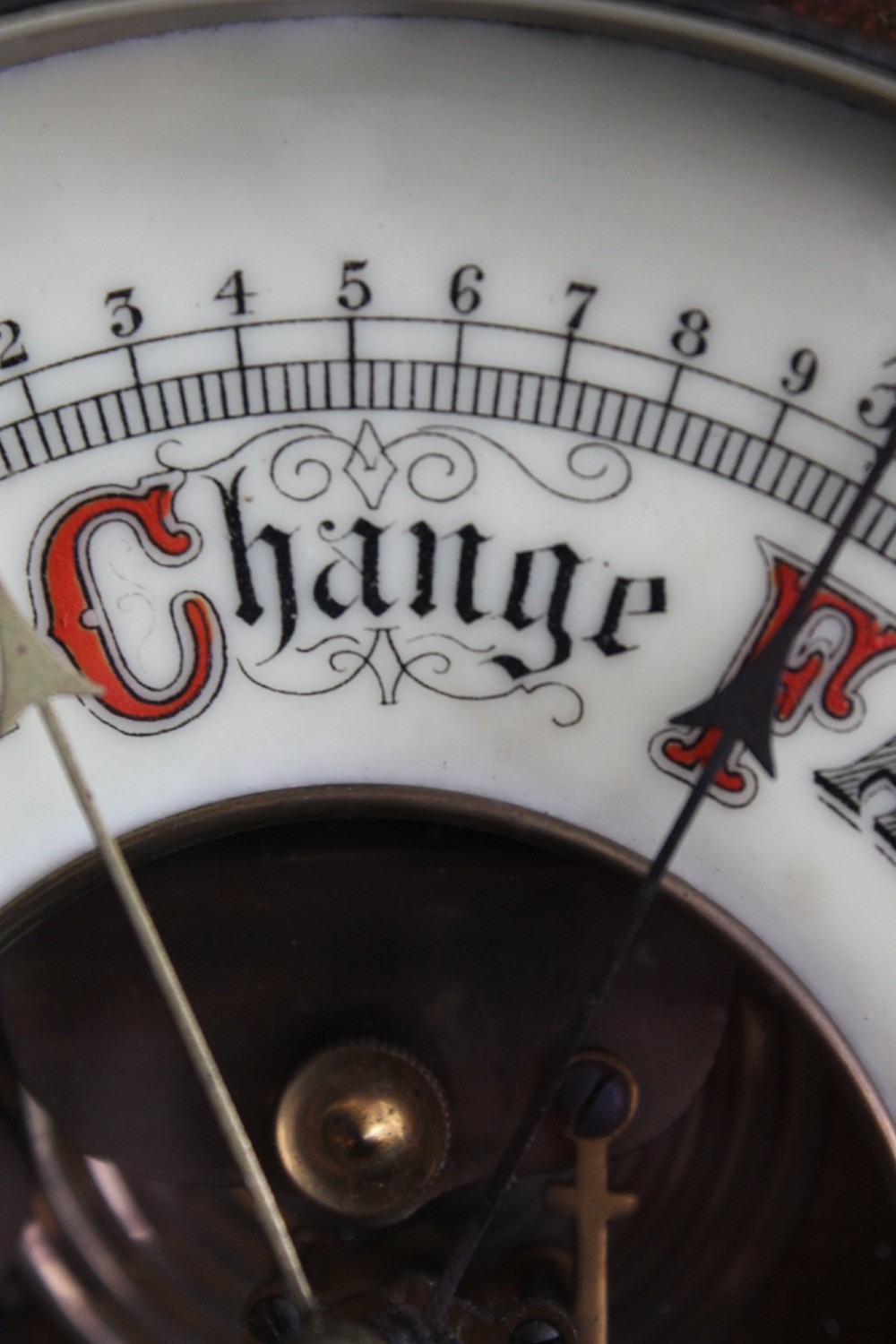 A circular Victorian walnut wall barometer featuring a carved wooden border, a brass hanging ring, and an exposed brass skeleton movement within an enamel dial. View VI