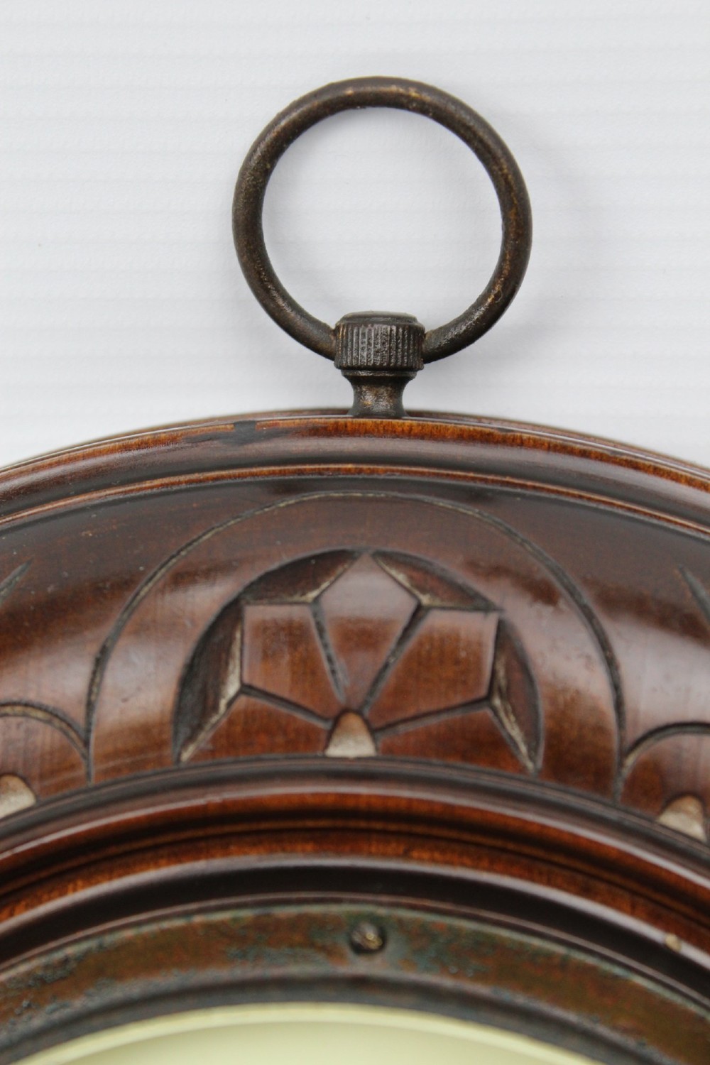 A circular Victorian walnut wall barometer featuring a carved wooden border, a brass hanging ring, and an exposed brass skeleton movement within an enamel dial. View VII